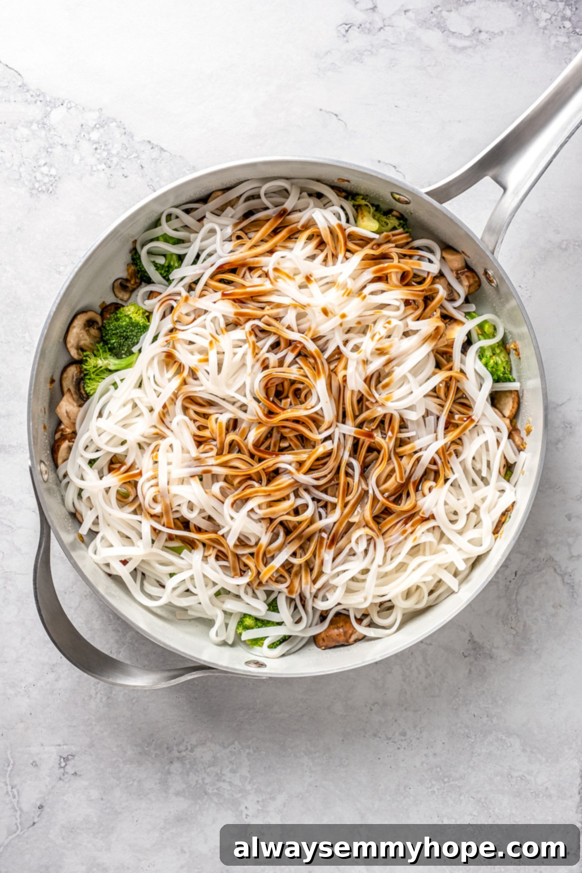 This vegan pad see ew pairs rice noodles, vegetables, and tofu with a sweet, savoury, and slightly tangy sauce for a restaurant-style meal! Overhead view of cooked noodles and the prepared sauce being added to the skillet with the vegetables.