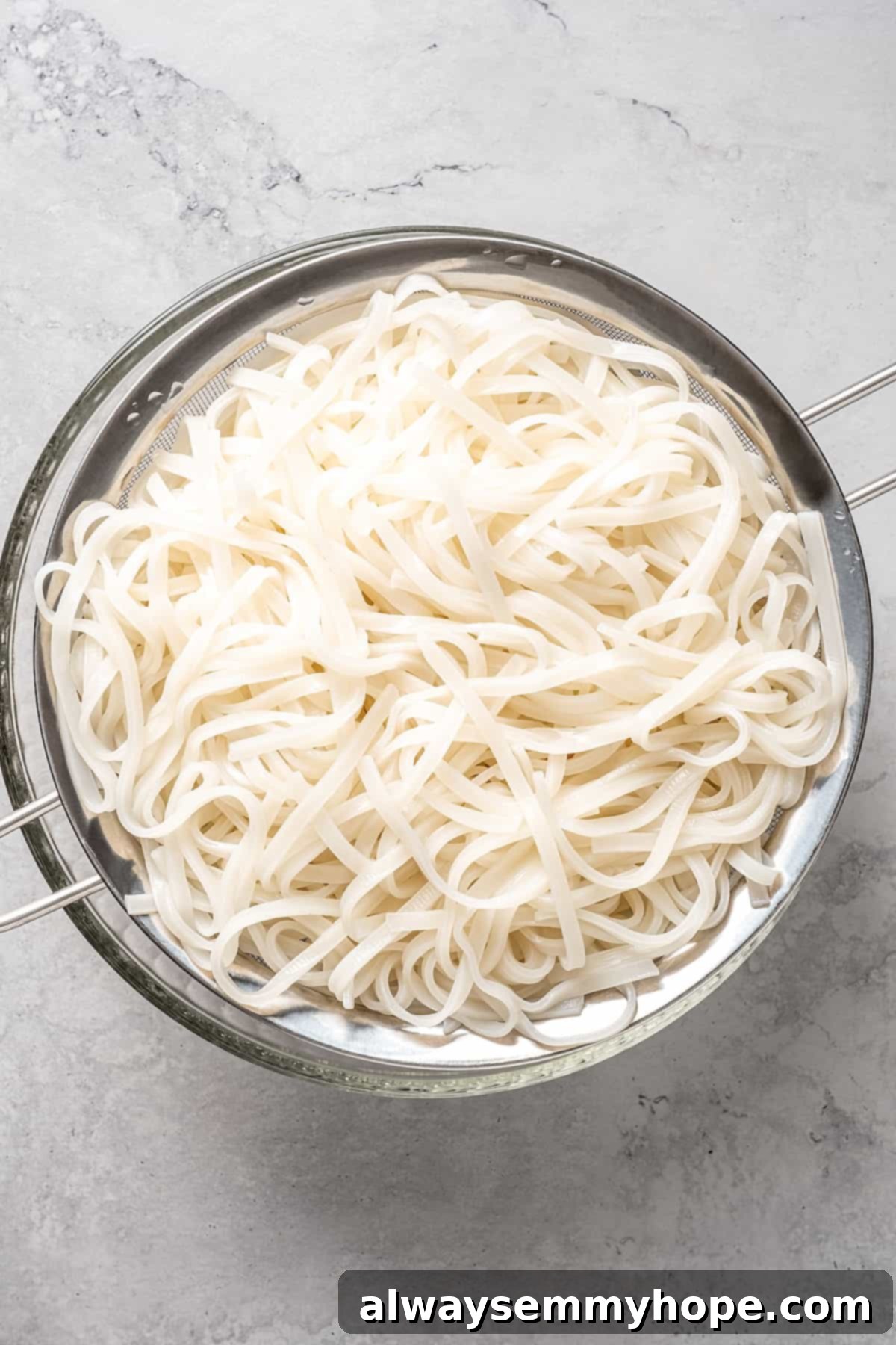 This vegan pad see ew pairs rice noodles, vegetables, and tofu with a sweet, savoury, and slightly tangy sauce for a restaurant-style meal! Overhead view of cooked rice noodles being drained in a colander.