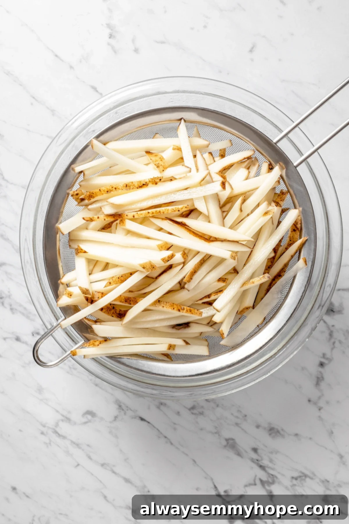 The air fryer makes these shoestring fries perfectly crispy without all the oil, and my blend of savoury seasonings makes them irresistible! Overhead view of straining fries in fine mesh strainer
