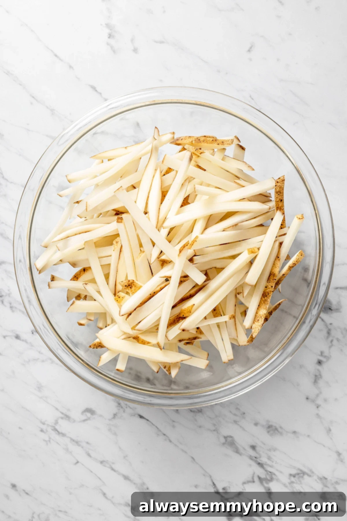 The air fryer makes these shoestring fries perfectly crispy without all the oil, and my blend of savoury seasonings makes them irresistible! Overhead view of uncooked fries in mixing bowl