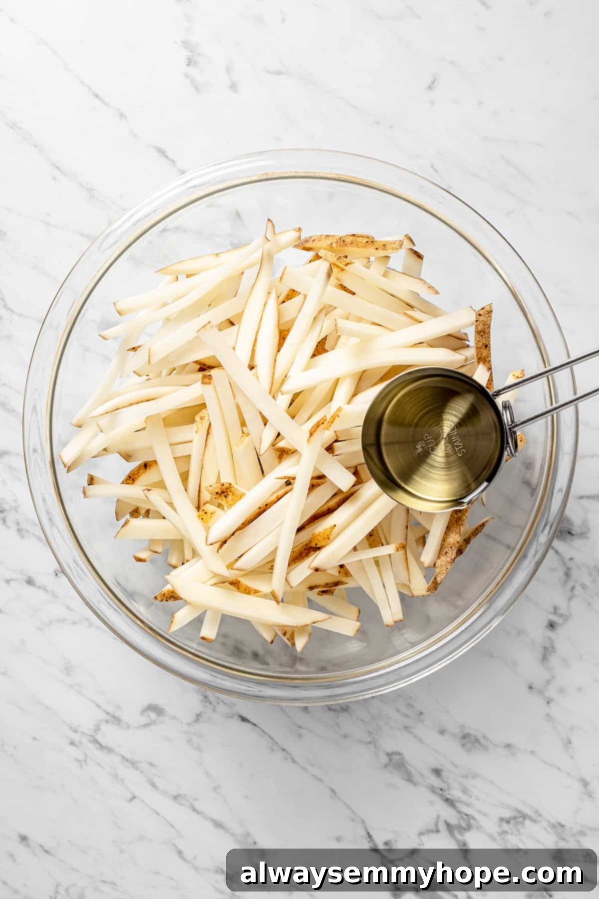 The air fryer makes these shoestring fries perfectly crispy without all the oil, and my blend of savoury seasonings makes them irresistible! Overhead view of uncooked fries in mixing bowl with oil