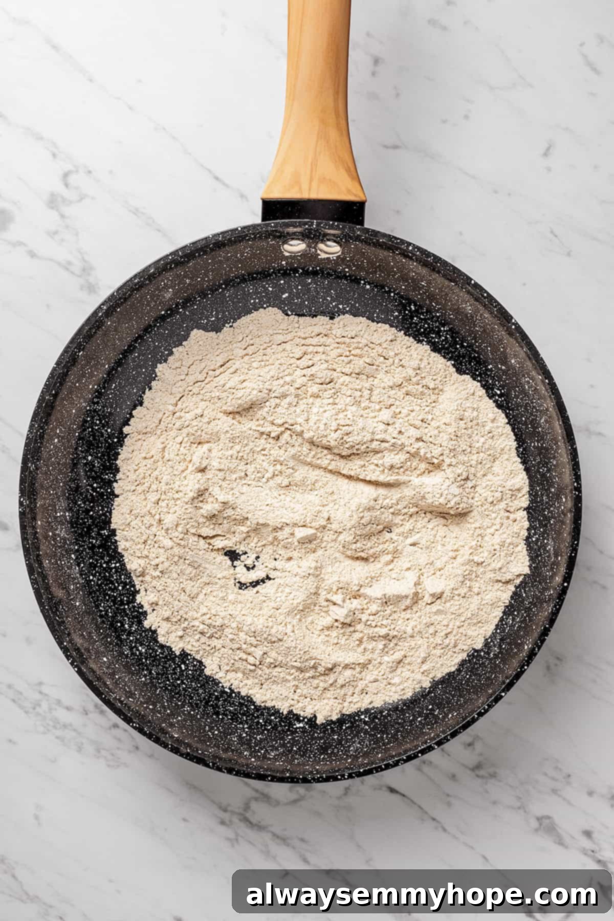 Toasting Oat Flour for Enhanced Flavor and Texture Overhead view of oat flour being toasted in a non-stick skillet over low heat, appearing slightly golden.