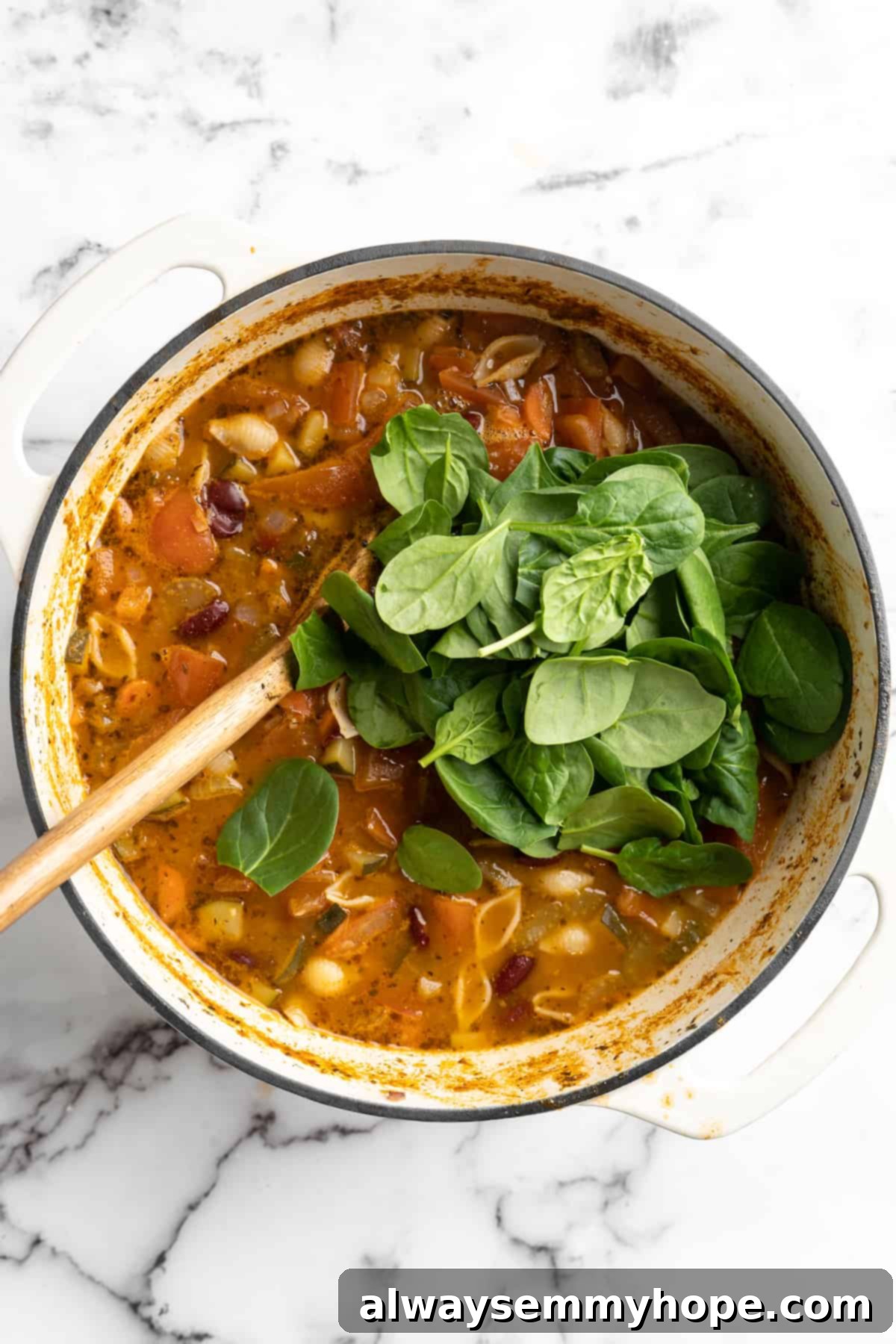 This vegetable minestrone soup is hearty comfort food at its best! Load it with veggies, beans, and pasta and enjoy a cozy one-pot meal. Overhead view of baby spinach added to pot of minestrone