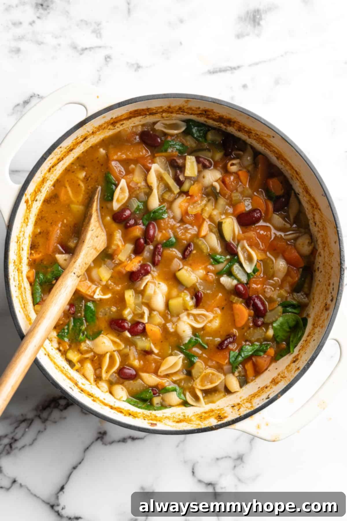 This vegetable minestrone soup is hearty comfort food at its best! Load it with veggies, beans, and pasta and enjoy a cozy one-pot meal. Overhead view of vegetable minestrone in pot with wooden spoon