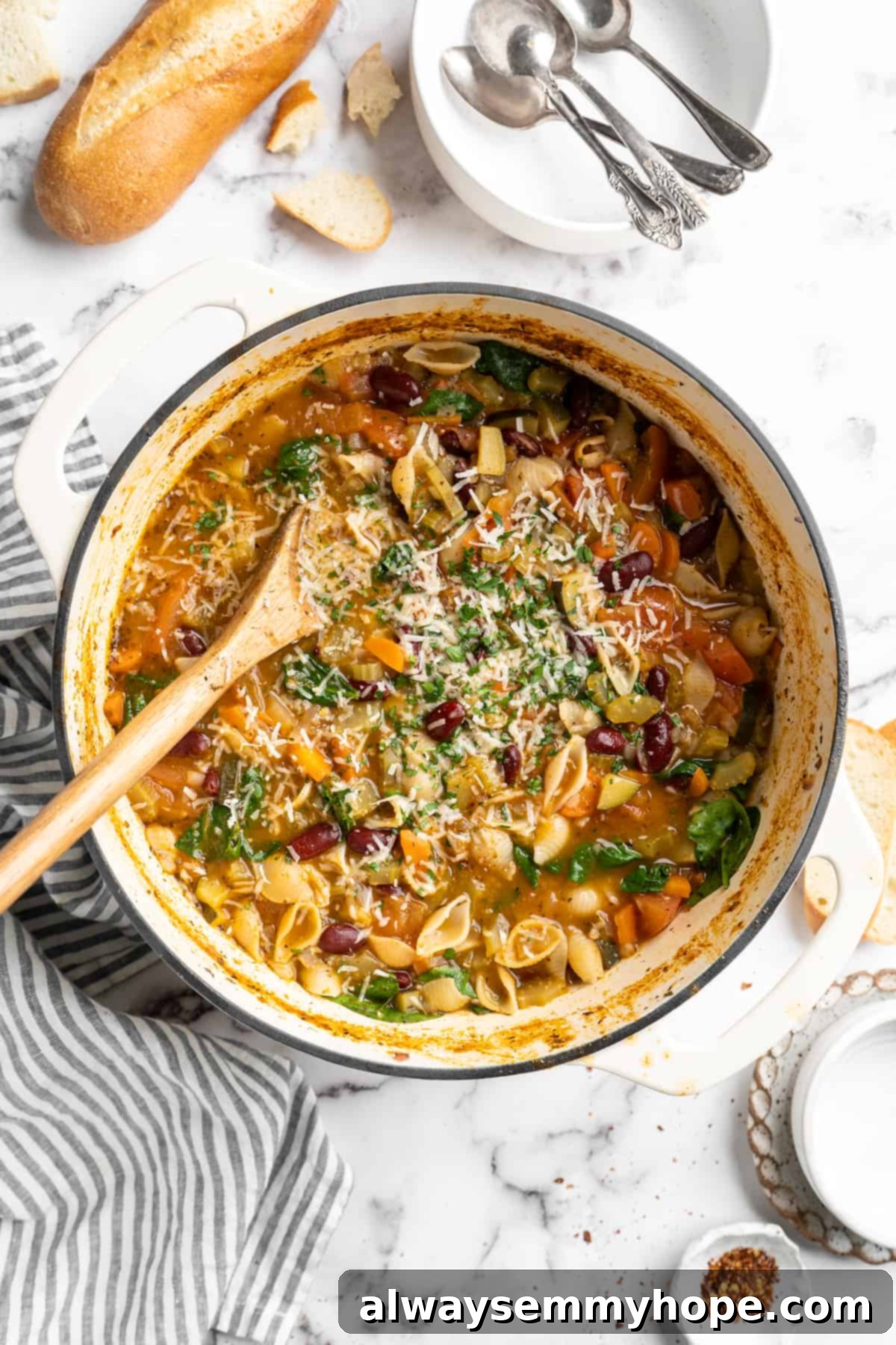 This vegetable minestrone soup is hearty comfort food at its best! Load it with veggies, beans, and pasta and enjoy a cozy one-pot meal. Overhead view of vegetable minestrone in pot with wooden spoon and vegan parmesan garnish