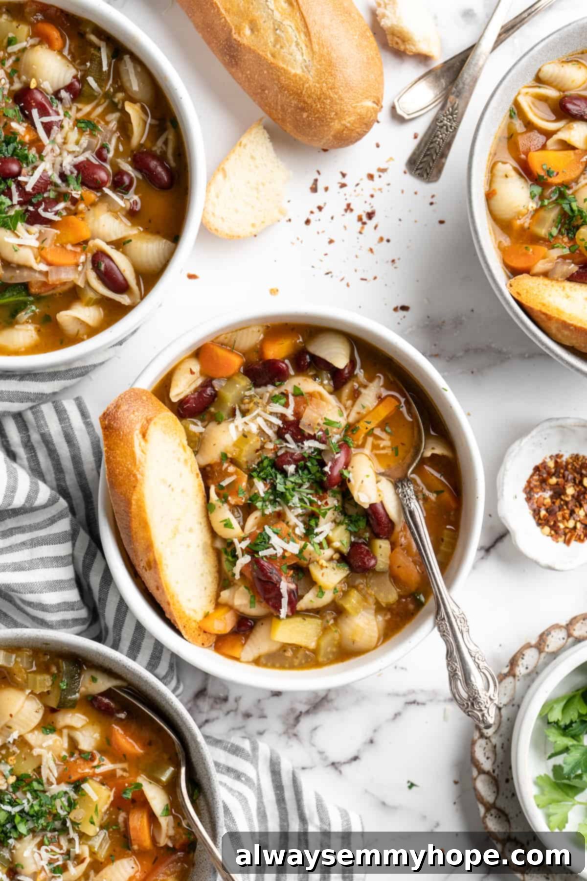 This vegetable minestrone soup is hearty comfort food at its best! Load it with veggies, beans, and pasta and enjoy a cozy one-pot meal. Overhead view of minestrone soup in bowls with bread and vegan parmesan