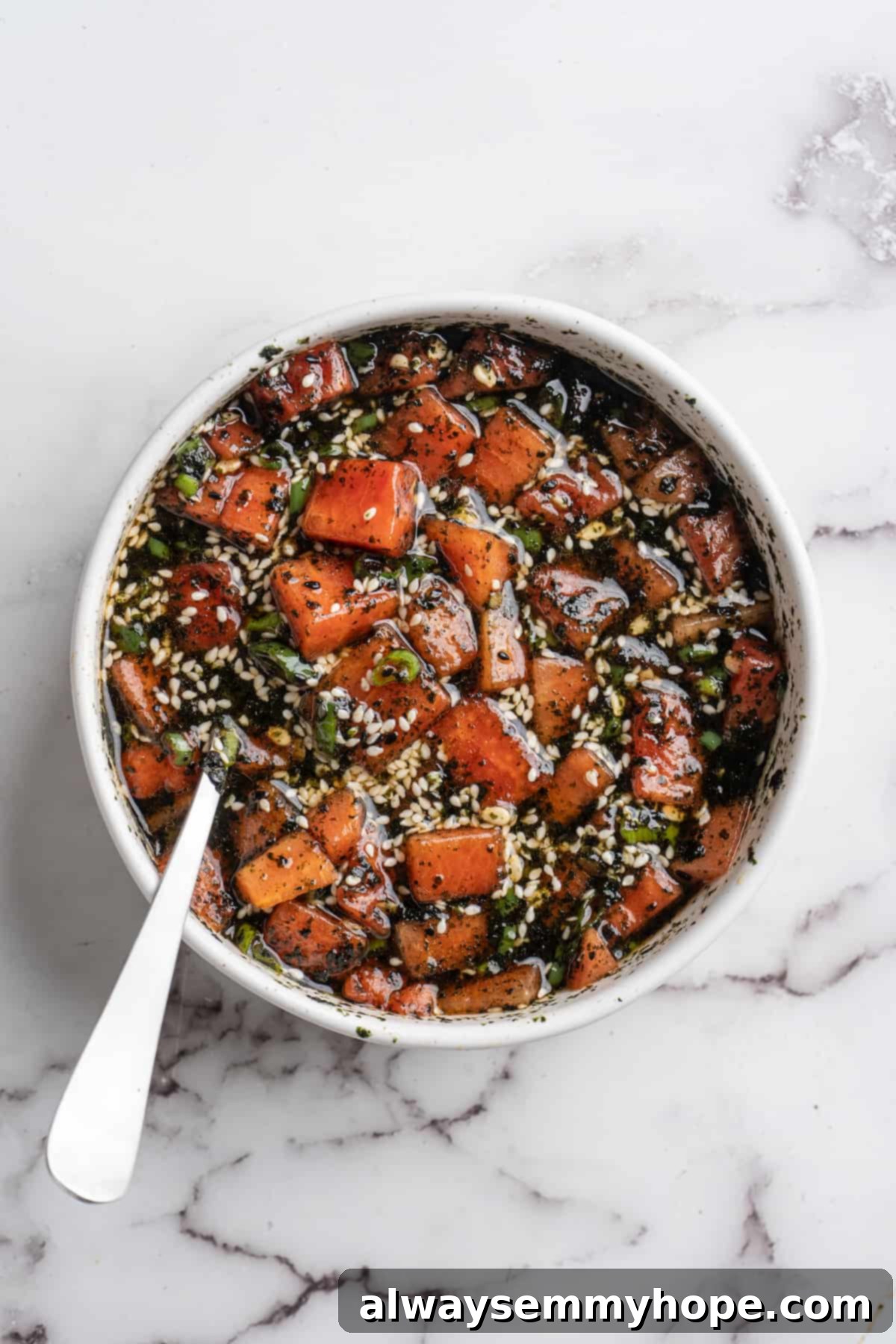 Witness the effortless process of transforming watermelon into a flavorful ahi tuna alternative, achieving a taste profile that's remarkably close to the real thing. Cubed vegan watermelon tuna marinating in a clear glass bowl, with a spoon nestled within, absorbing the rich flavors of the seasoning blend.