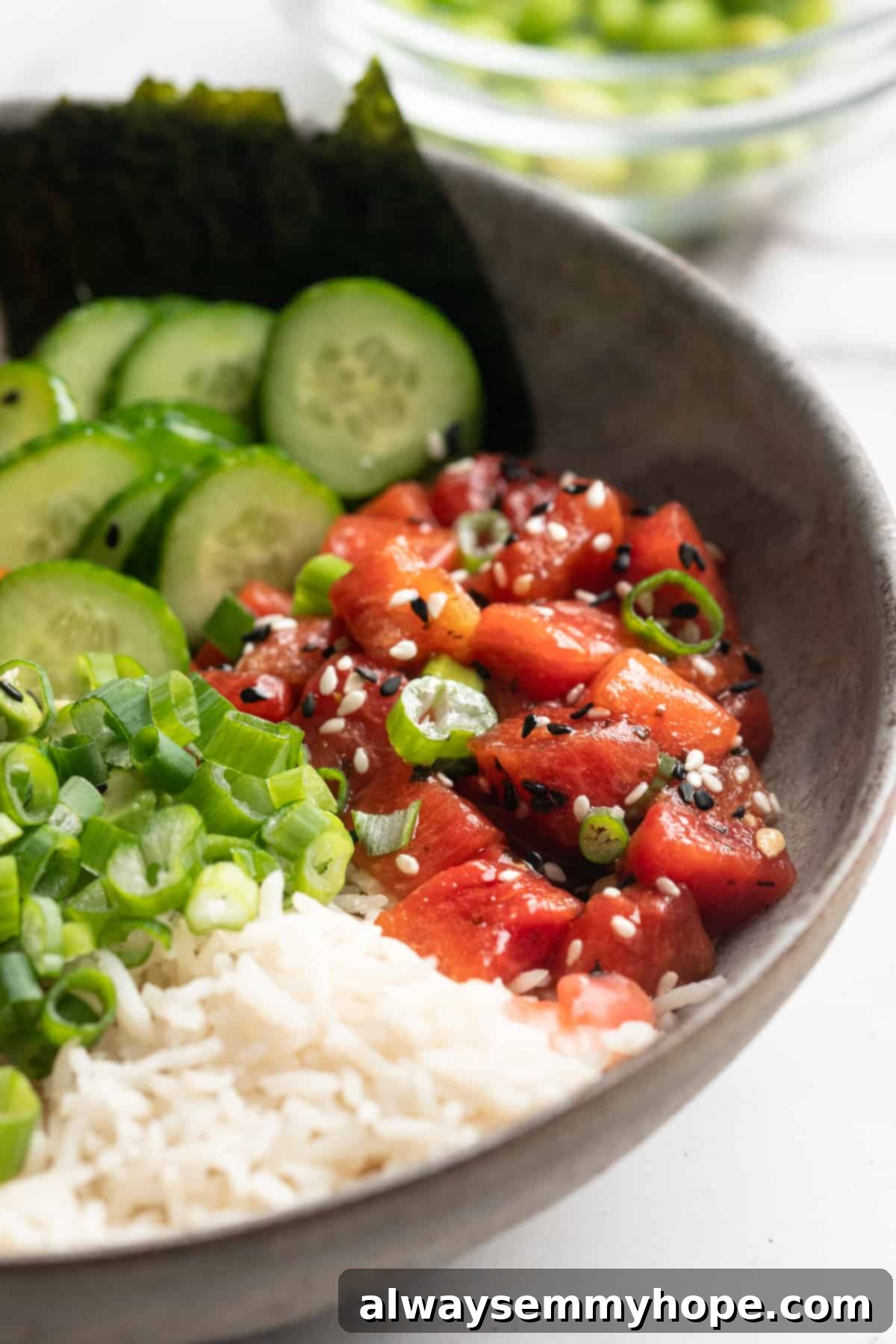 Create stunning and delicious vegan poke bowls with ease, using our transformative watermelon tuna recipe that perfectly complements rice and fresh vegetables. A delectable vegan poke bowl featuring watermelon tuna, fluffy sushi rice, crisp cucumber ribbons, and a sprinkle of fresh green onions, ready to be enjoyed.