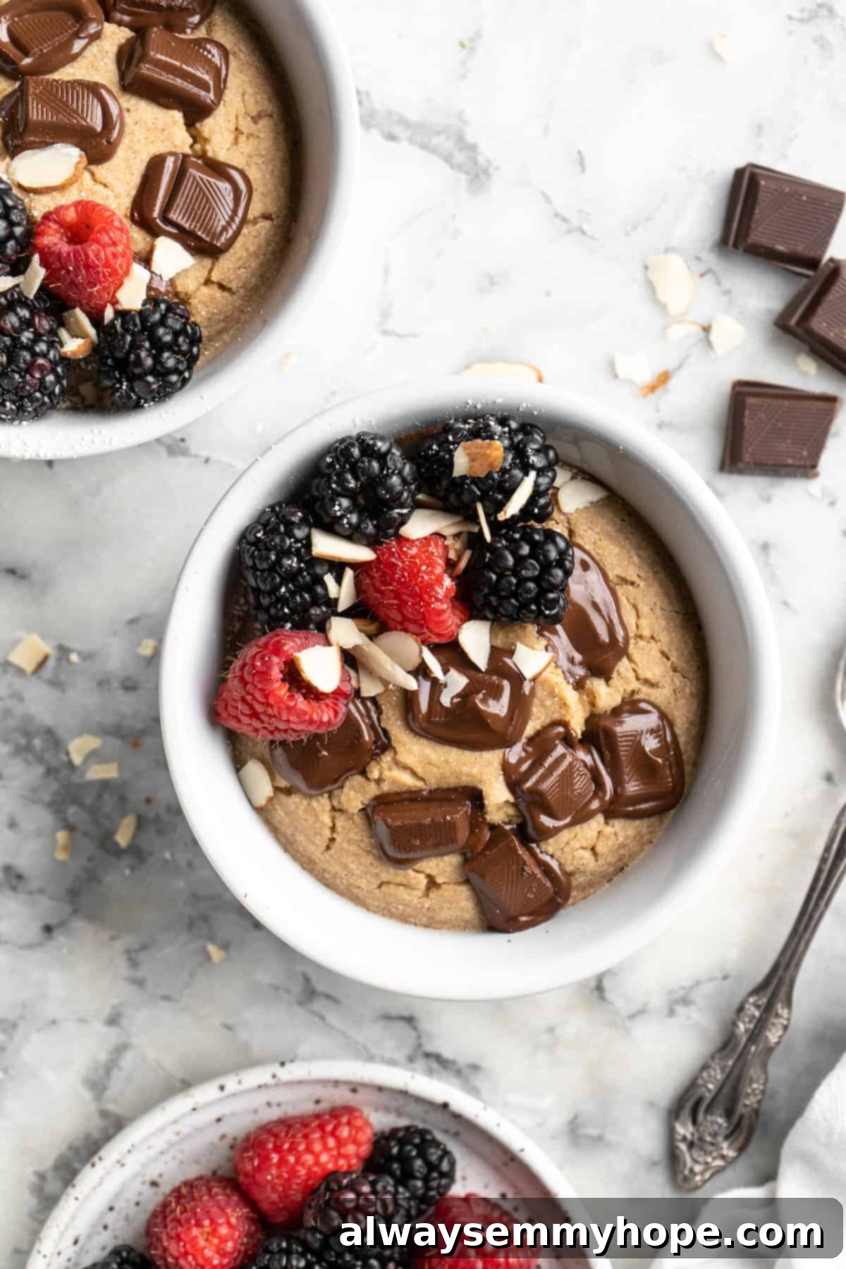 These TikTok vegan baked oats are a filling breakfast, with just a little bit of decadence thanks to the addition of dark chocolate. So easy! Overhead view of two bowls of vegan baked oats topped with chocolate, berries, and sliced almonds