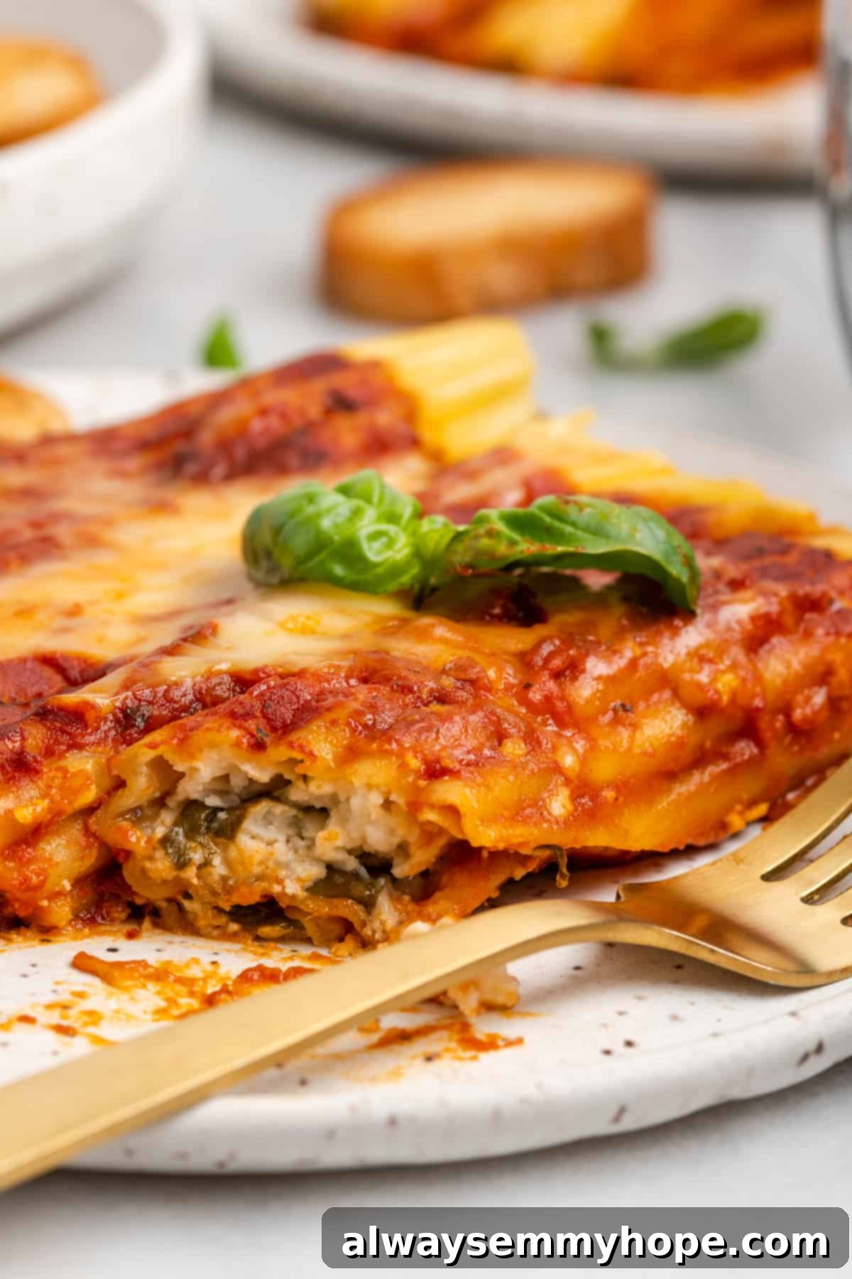 Delicious vegan manicotti served on a plate, garnished with basil and ready to eat. A serving of vegan manicotti on a white plate, elegantly garnished with fresh basil, ready to be enjoyed with a gold fork.