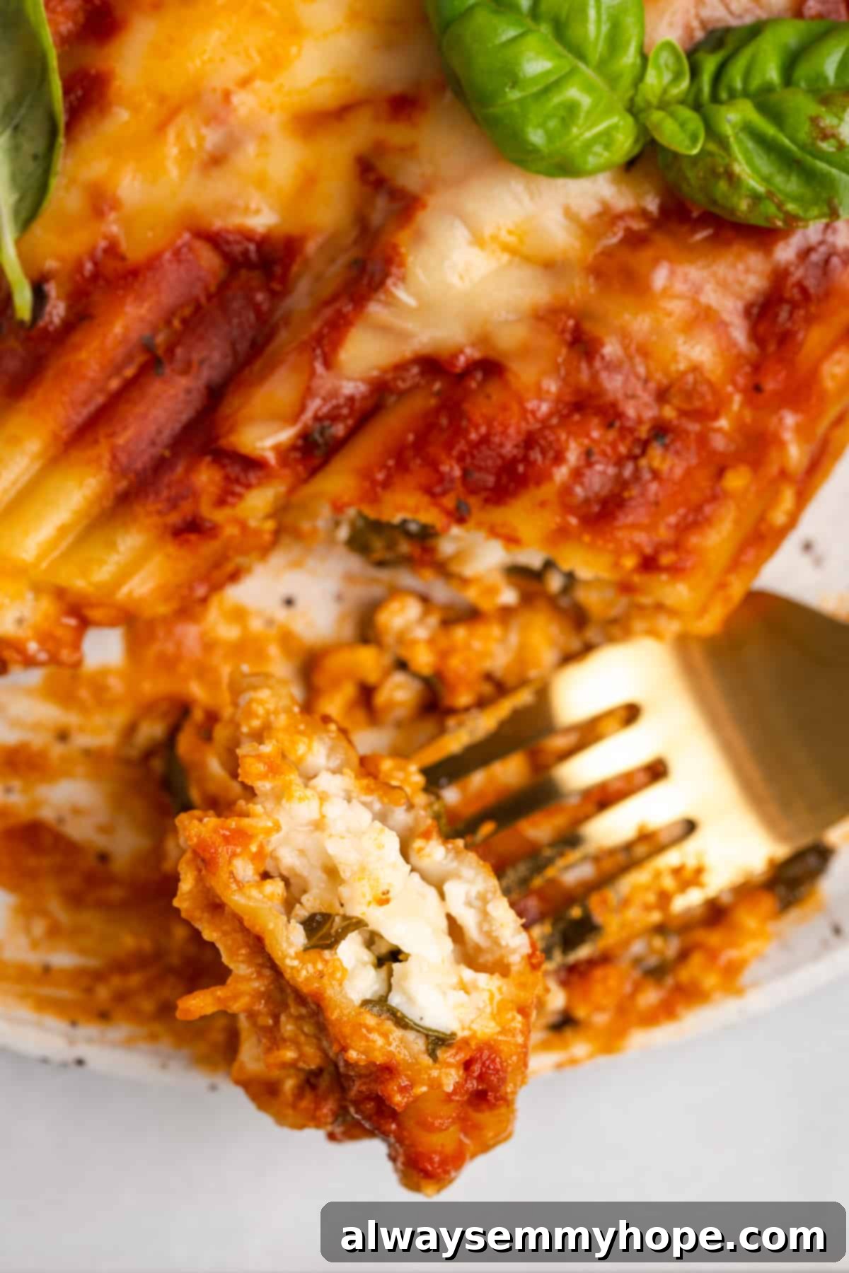 A perfect forkful of vegan manicotti, highlighting its creamy spinach ricotta filling. A close-up shot of a fork lifting a perfect bite of vegan manicotti, showcasing the cheesy, spinach-filled interior.