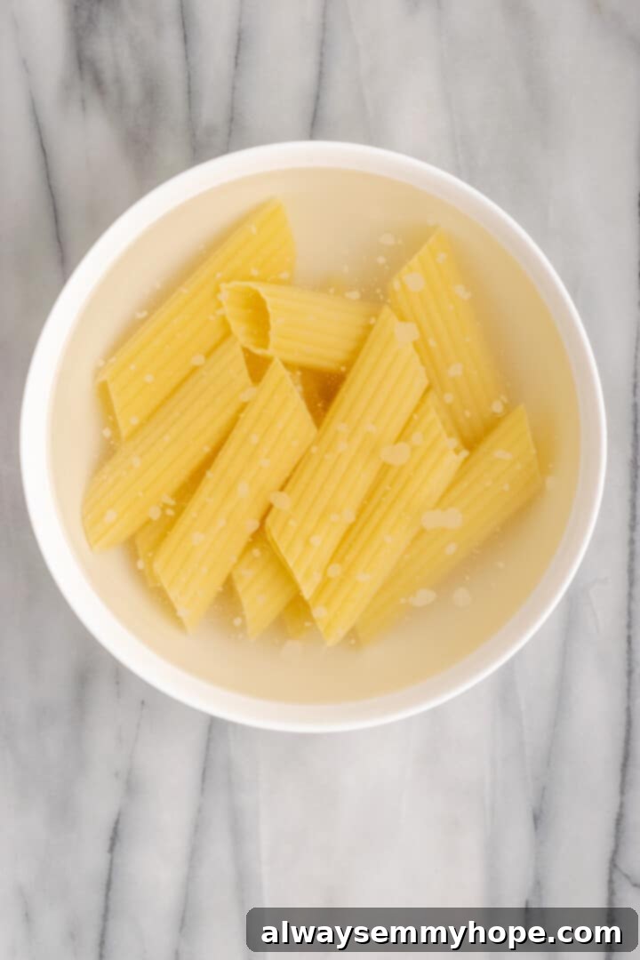 Soaking manicotti shells in hot water for a perfect no-boil preparation. Manicotti pasta shells soaking in a bowl of hot water, a crucial step for the no-boil method to soften them before filling.