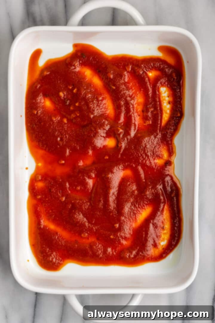 Spreading a layer of delicious pasta sauce in the baking dish for the manicotti. A baking dish with a base layer of savory pasta sauce, ready to receive the stuffed manicotti shells.