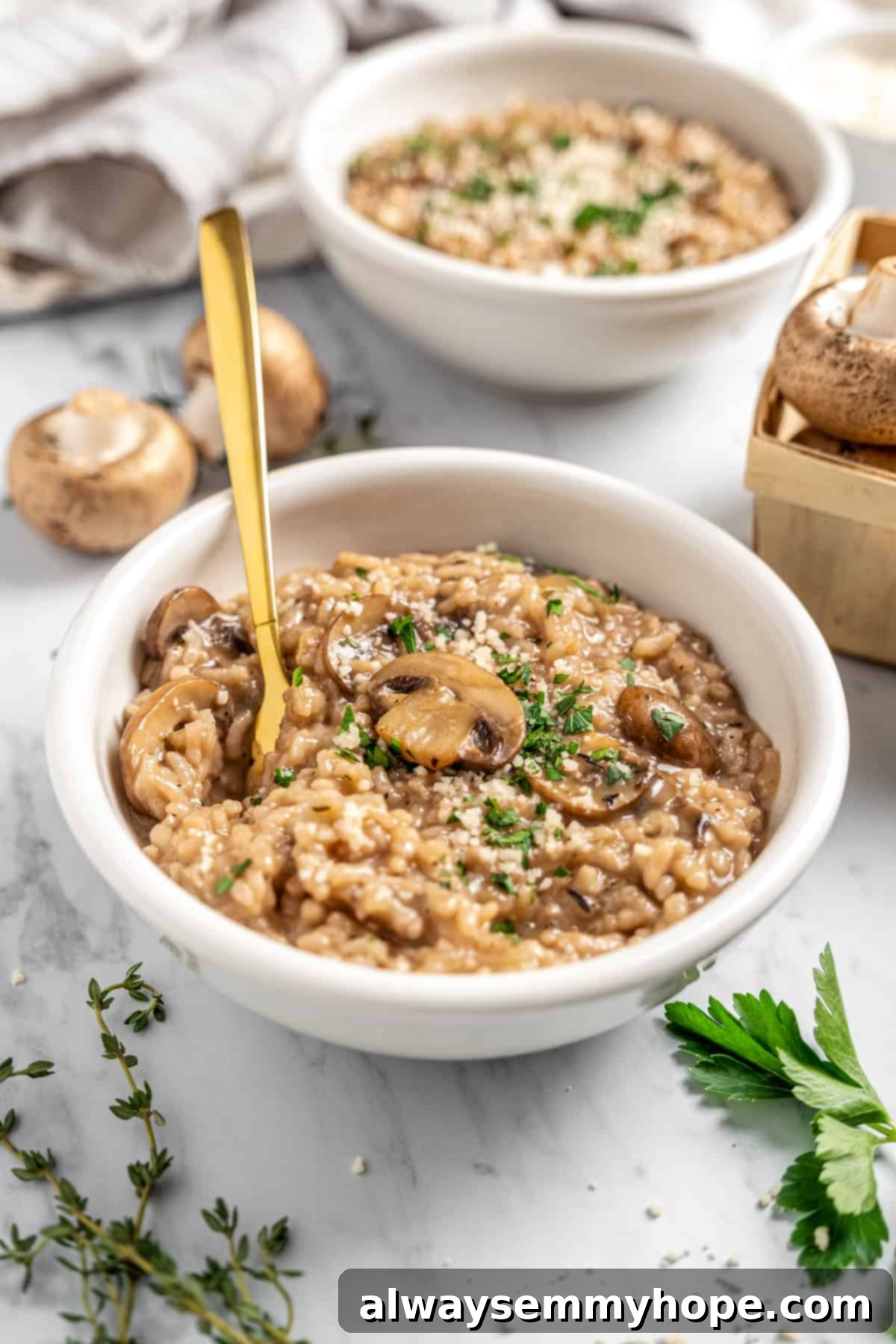 Two bowls of vegan Instant Pot risotto with mushrooms, garnished with fresh herbs, with additional fresh herbs and mushrooms artfully arranged on a tabletop