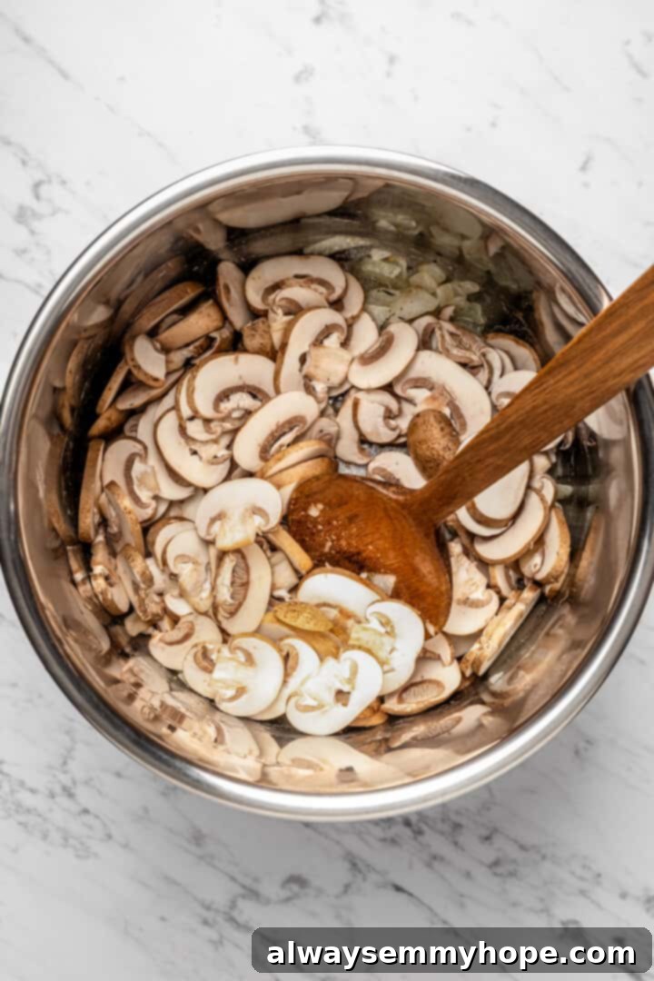 Overhead view of a wooden spoon gently stirring sliced mushrooms into the fragrant onion and garlic mixture in the Instant Pot insert