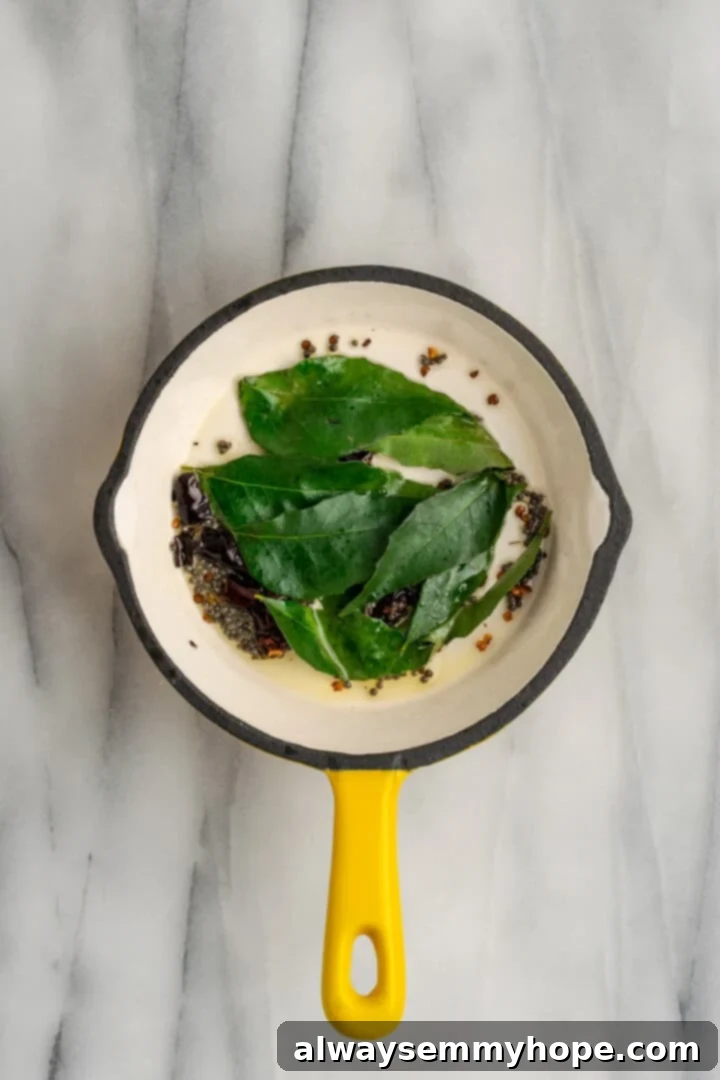 This vegan sambar is just like the sambar at your favourite Indian restaurant! Here's how to make this hearty lentil and veggie stew at home. Overhead view of fresh curry leaves added to small saucepan of tempering