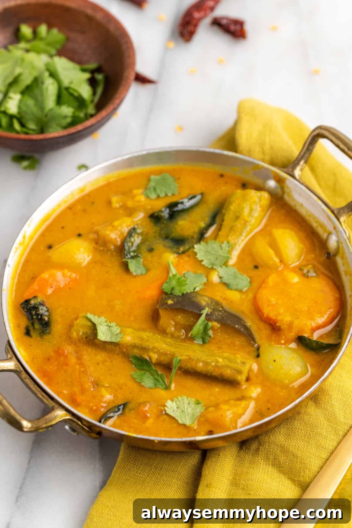 This vegan sambar is just like the sambar at your favourite Indian restaurant! Here's how to make this hearty lentil and veggie stew at home. Vegan sambar in gold serving dish, with cilantro leaves scattered on top for garnish