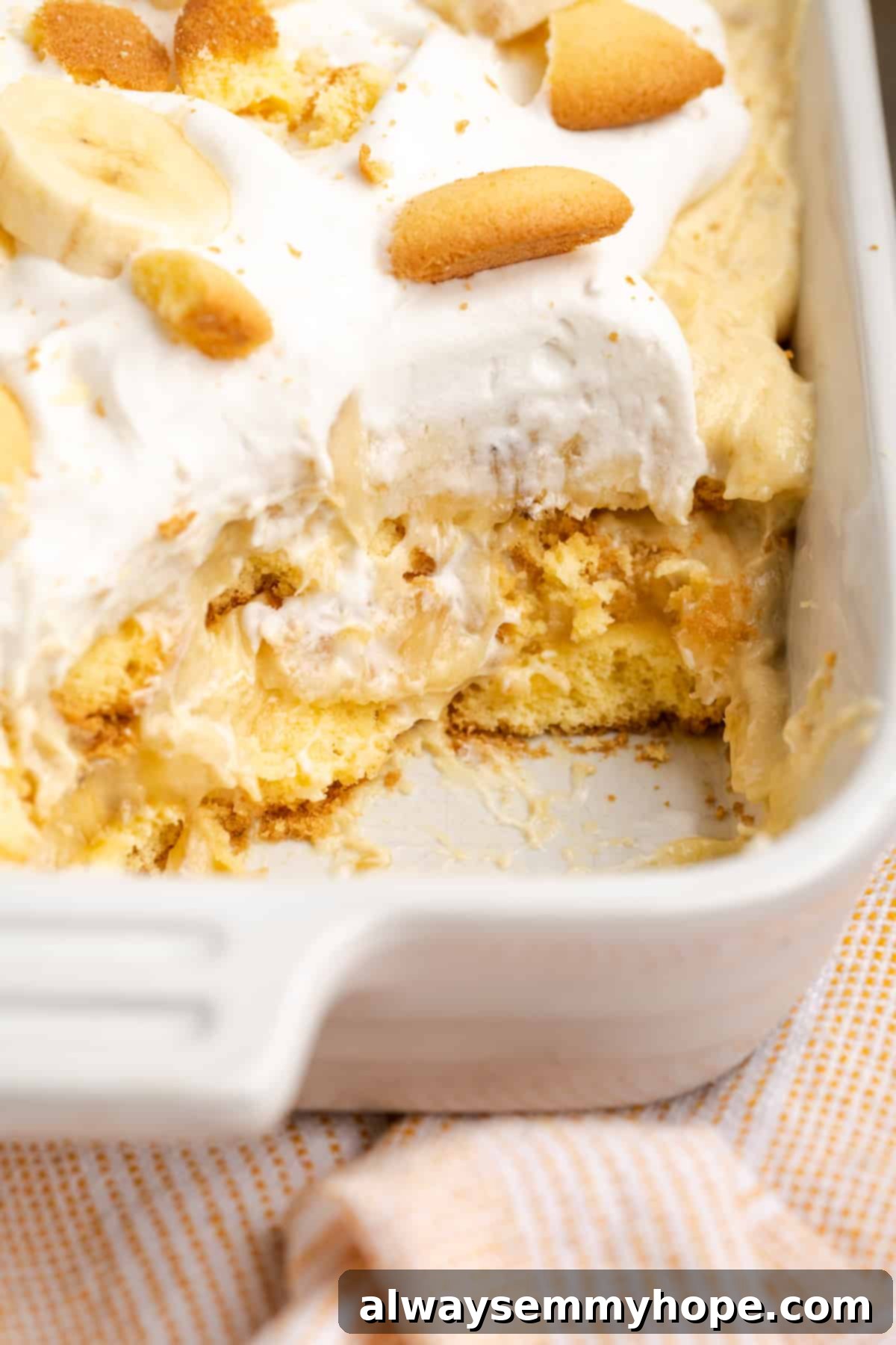 Vegan banana pudding in baking dish, with a serving removed to clearly show the creamy layers of pudding, bananas, and wafers