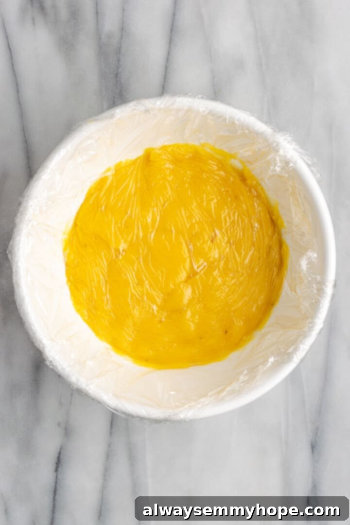 Banana pudding in mixing bowl with plastic wrap pressed into top for chilling