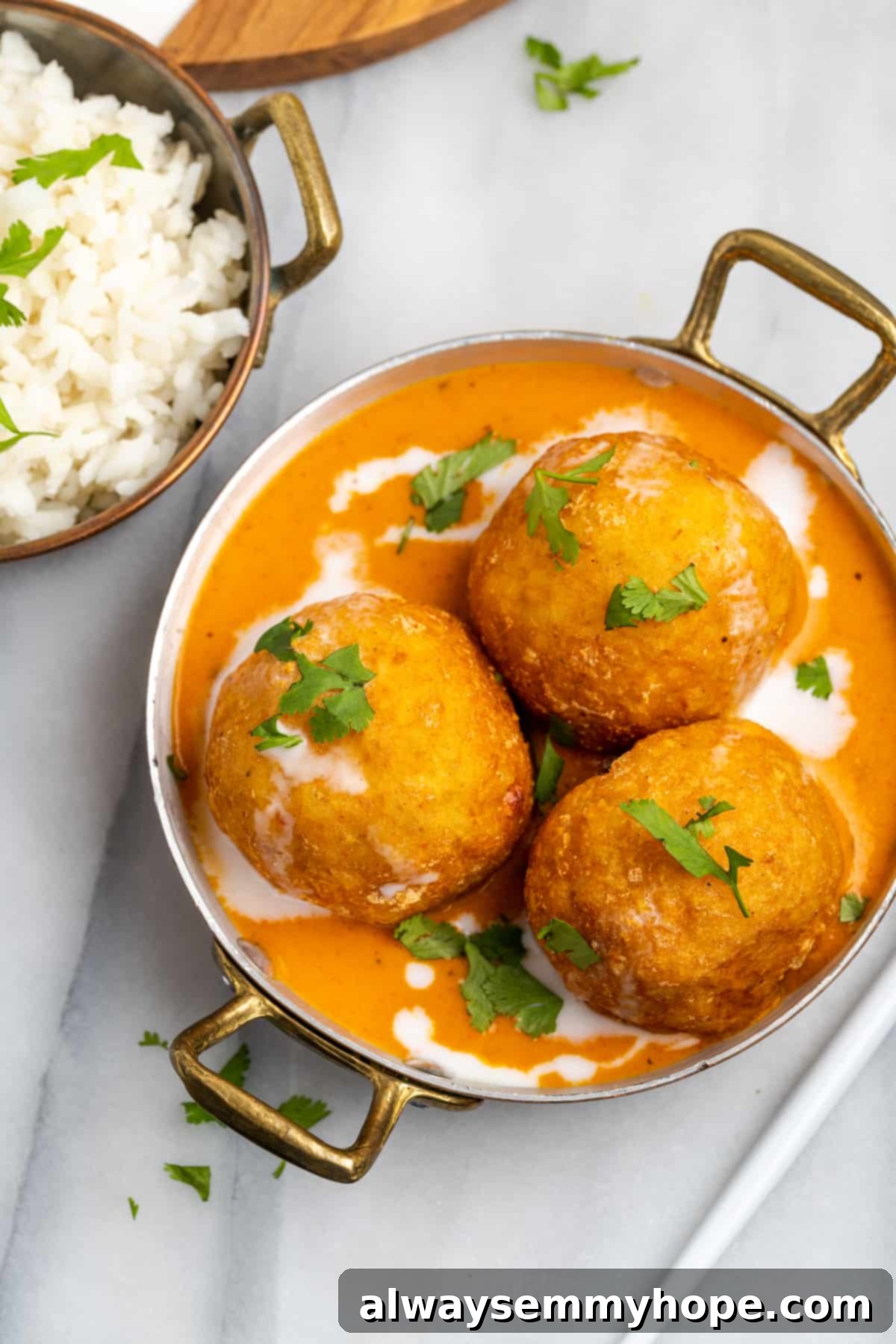 Overhead view of malai kofta in gold serving bowl with cooked rice in second bowl