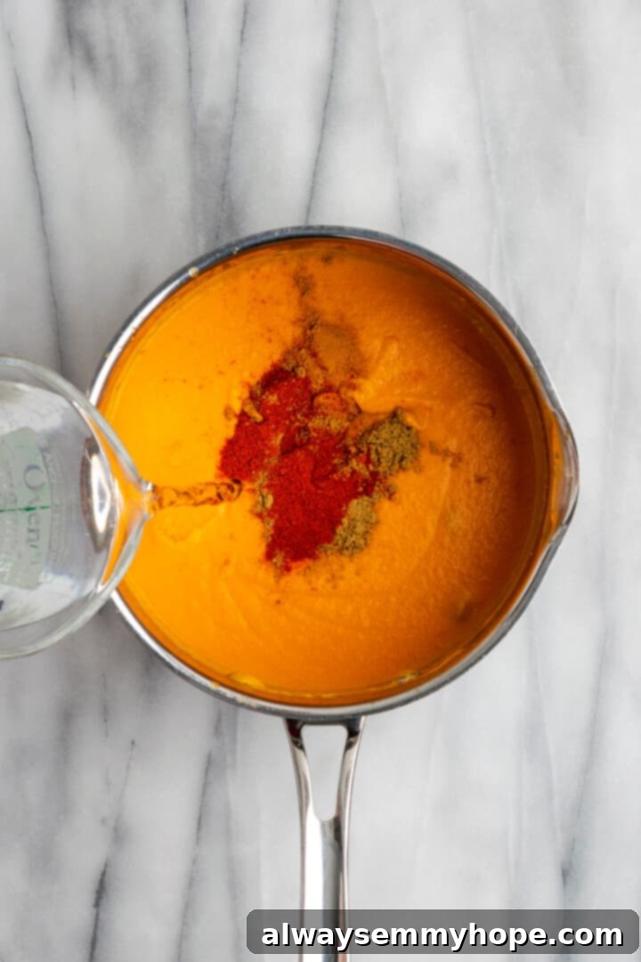 Pouring water and adding spices to malai kofta sauce in pan