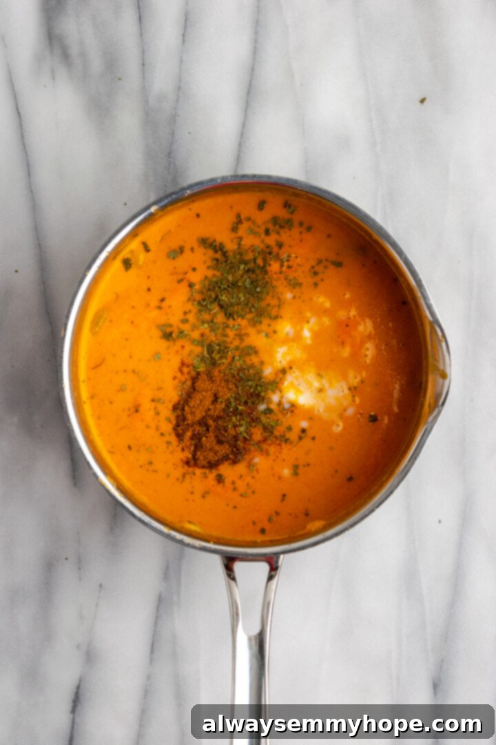Overhead view of spices added to malai kofta sauce in pan