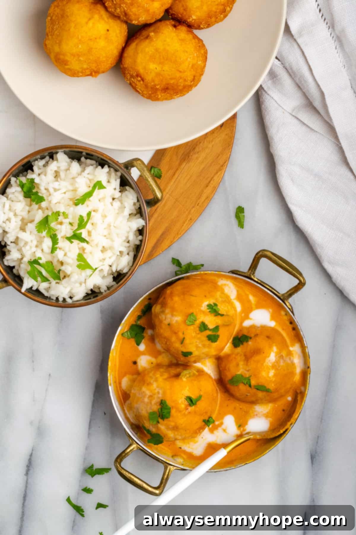 Overhead view of malai kofta in bowl with sauce, with bowl of rice and dumplings