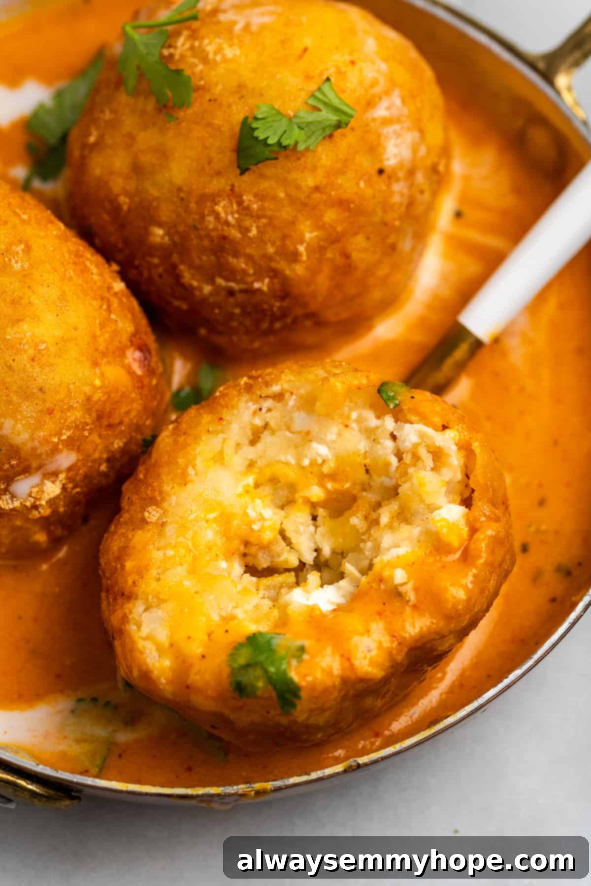 Malai kofta in bowl with sauce, with dumpling cut into to show inside