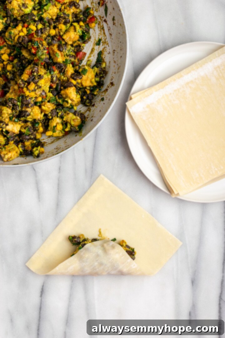 These crispy vegan southwest egg rolls are full of bold flavors and satisfying ingredients like vegan chicken, black beans, and veggies. Yum! Rolling up egg roll wrapper around filling