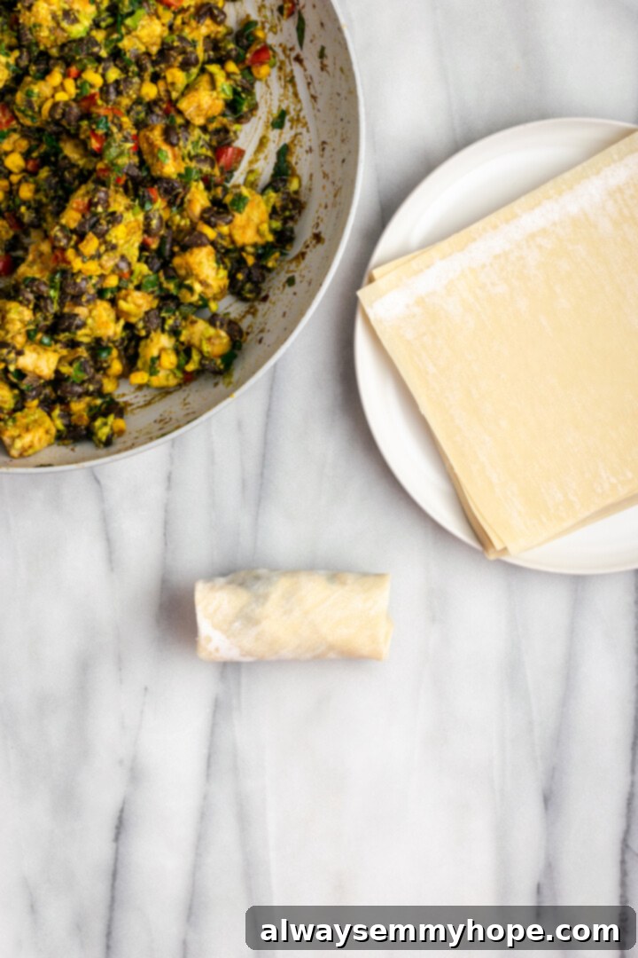 Overhead view of rolled southwest egg roll, plate of egg roll wrappers, and filling