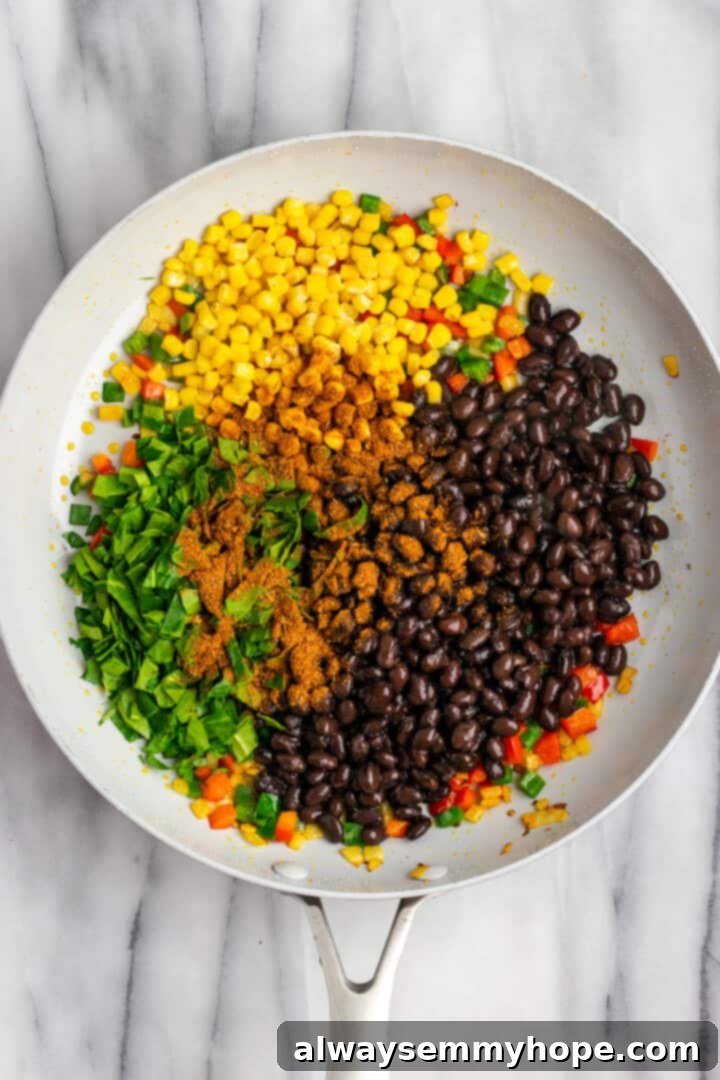 These crispy vegan southwest egg rolls are full of bold flavors and satisfying ingredients like vegan chicken, black beans, and veggies. Yum! Overhead view of vegetables and beans for vegan southwest egg roll filling in skillet