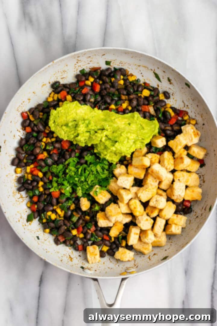 These crispy vegan southwest egg rolls are full of bold flavors and satisfying ingredients like vegan chicken, black beans, and veggies. Yum! Overhead view of ingredients for vegan southwest egg roll filling in skillet
