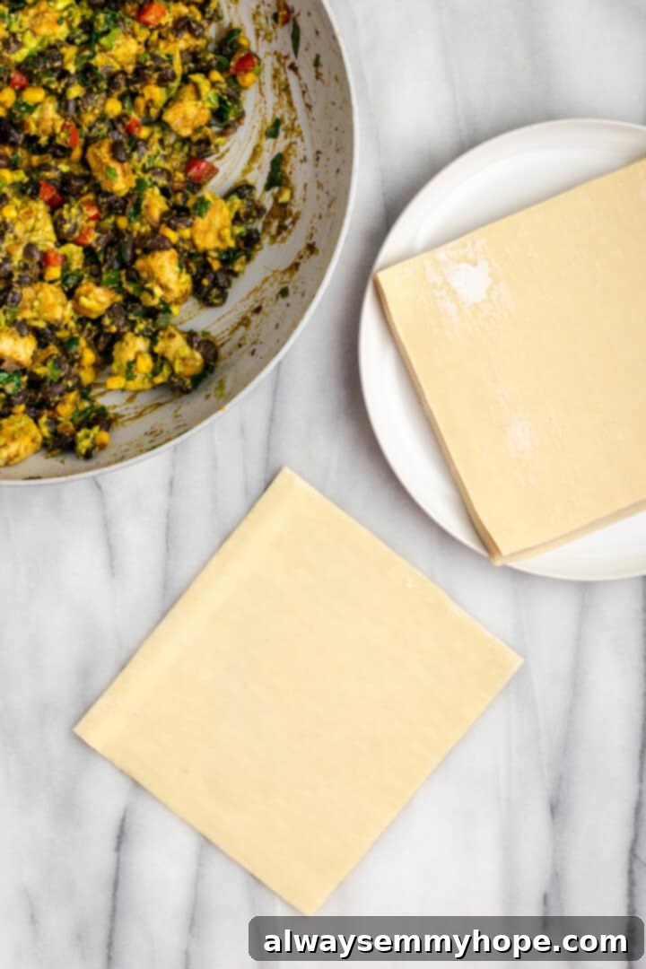 These crispy vegan southwest egg rolls are full of bold flavors and satisfying ingredients like vegan chicken, black beans, and veggies. Yum! Egg roll wrapper set on countertop, with filling and additional wrappers in background