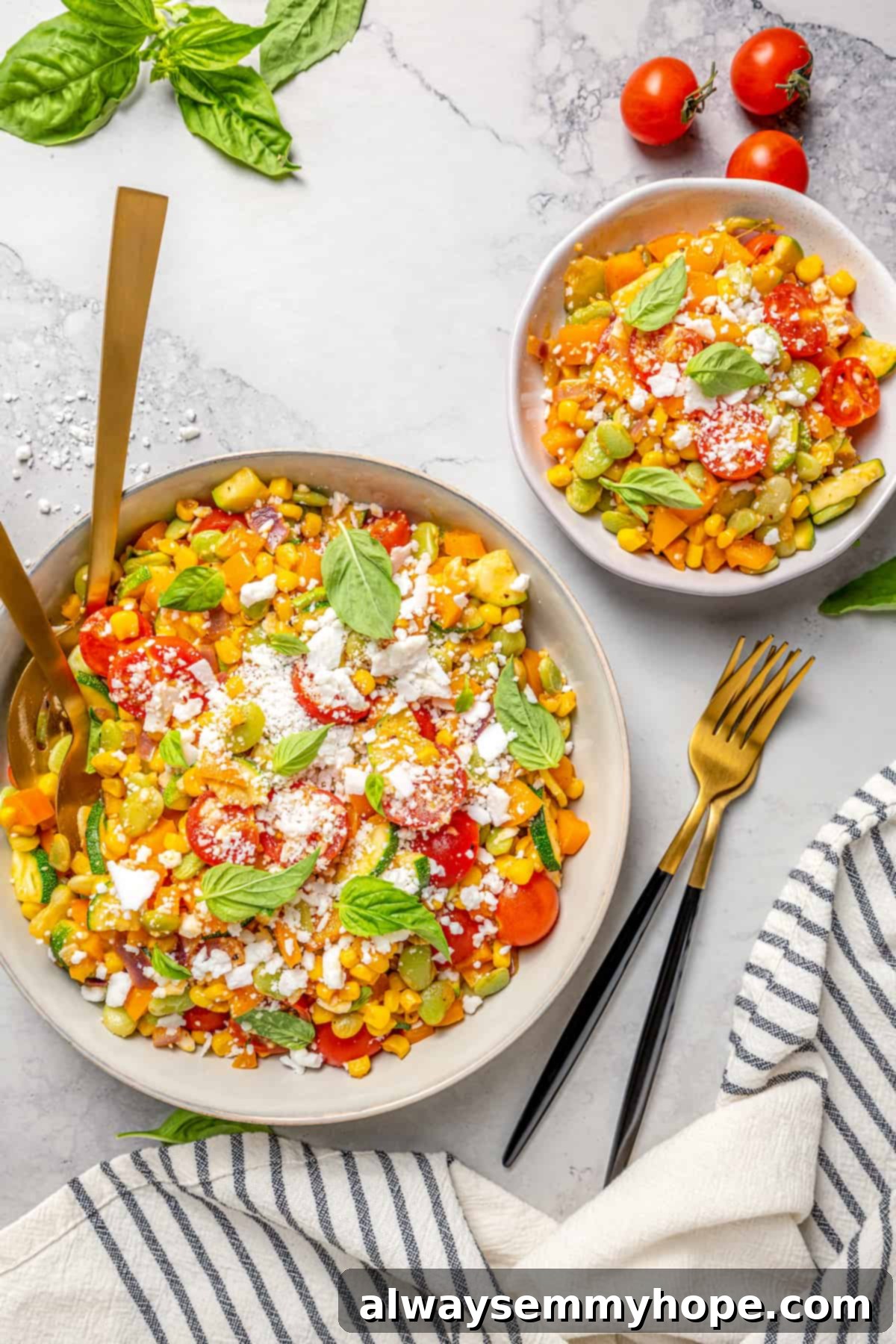 Overhead view of two bowls of corn succotash with forks, kitchen towel tomatoes, and basil