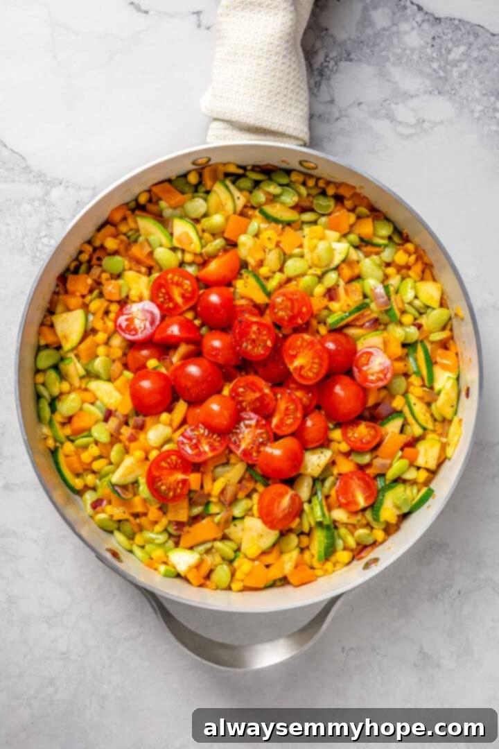 Overhead view of vegan corn succotash in skillet after adding tomatoes