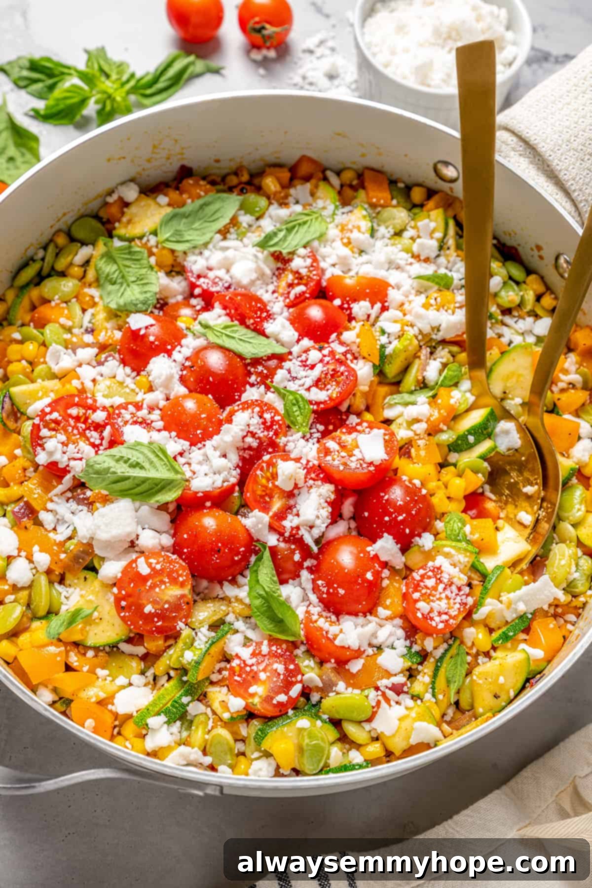 Skillet of vegan corn succotash topped with cherry tomatoes, feta, and basil