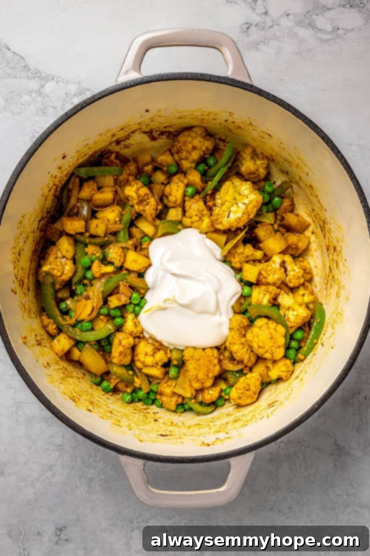 Adding Vegan Yogurt for Creaminess and Tang A scoop of plain vegan yogurt added to the cooked vegetables and spices in the pot.