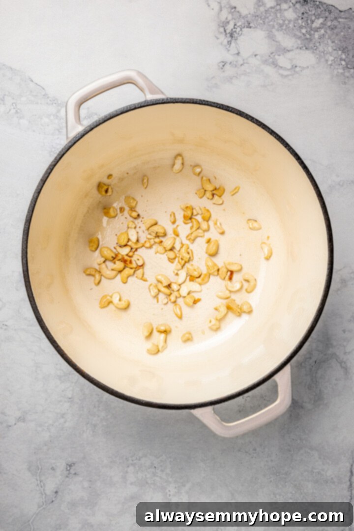 Toasting Cashews for Vegan Vegetable Biryani Raw cashew pieces toasting in a pot with a small amount of oil.