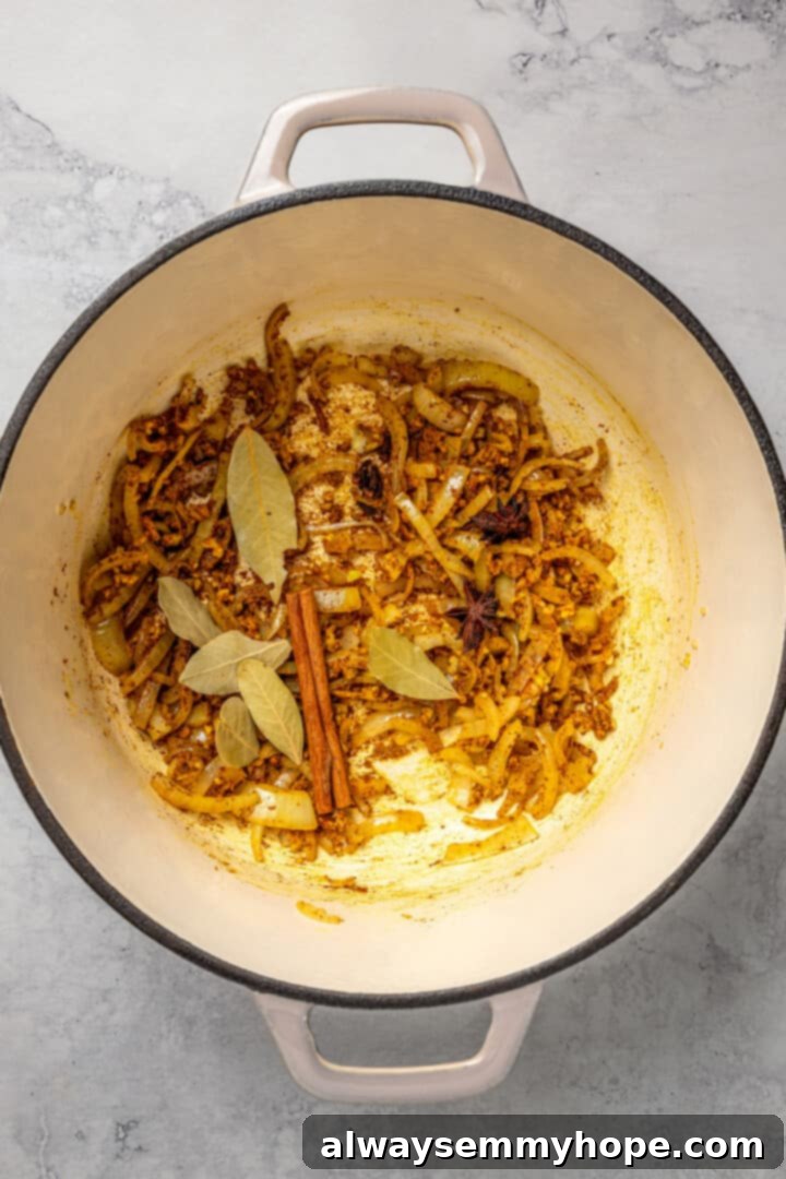 Blooming Aromatic Spices for Biryani Various whole and ground spices, including cinnamon stick, cloves, bay leaves, and turmeric, blooming with onions in a pot.