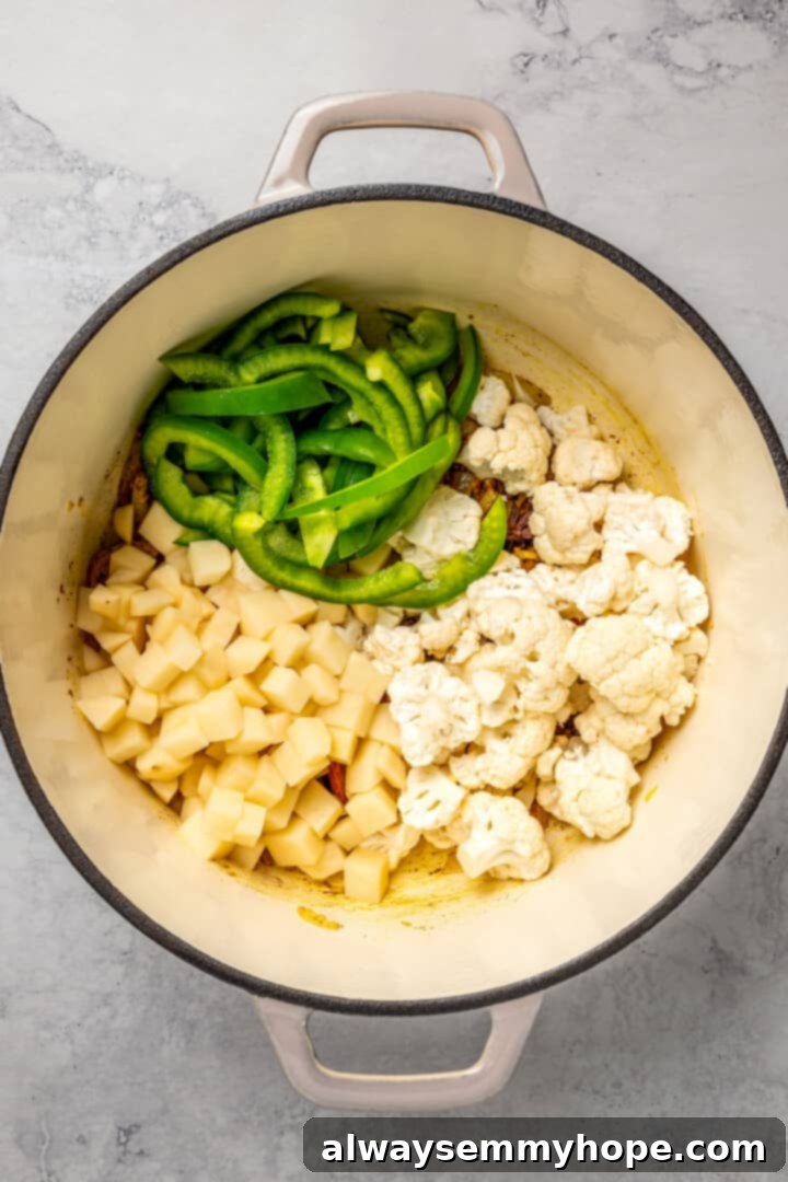 Adding Fresh Vegetables to Biryani Spice Base Cubed potatoes, cauliflower florets, and strips of green bell pepper added to a pot with sautéed onions and spices.