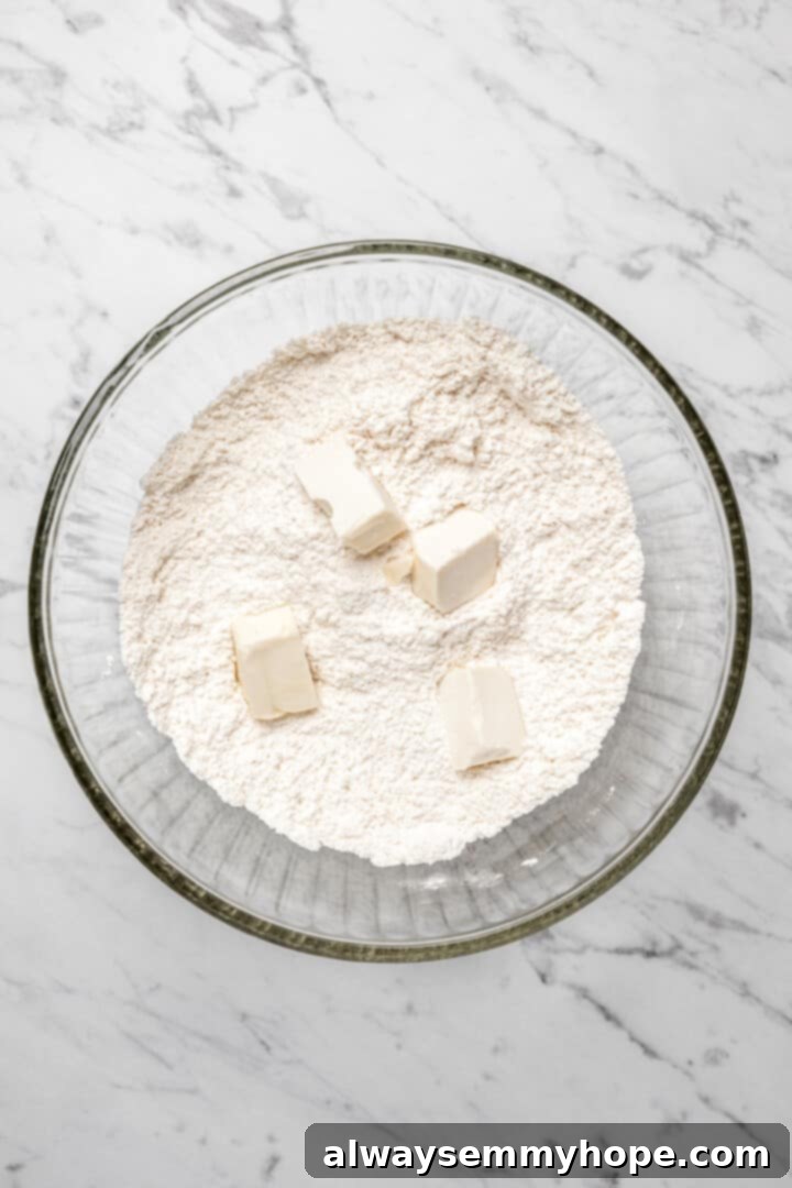 Overhead view of cubed butter added to glass mixing bowl with dry dumpling ingredients
