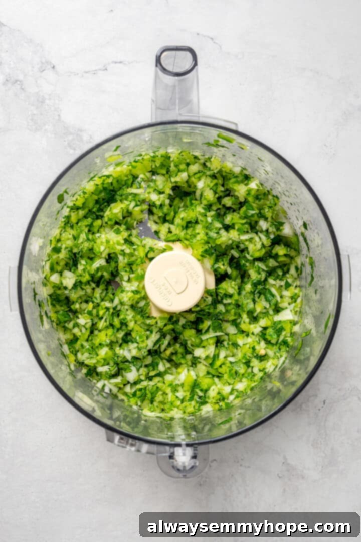 Overhead view of the sofrito mixture in a food processor after pulsing, resembling a chunky salsa.