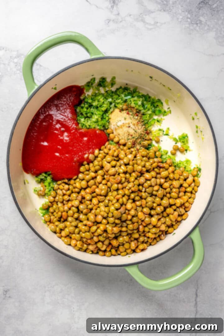 Overhead view of tomato sauce, green pigeon peas, and various spices being added to the cooked sofrito in an enamel Dutch oven.