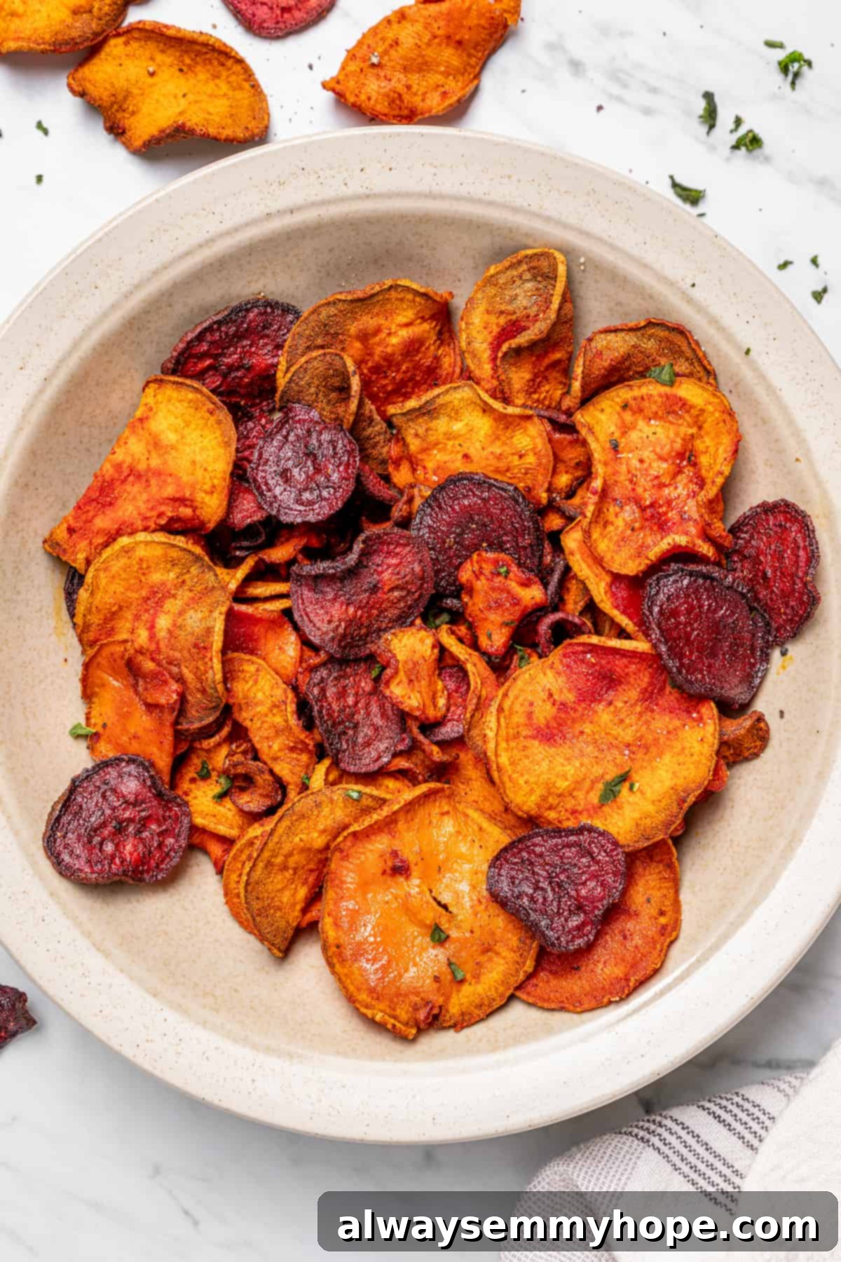 A beautifully arranged bowl of crispy air fryer veggie chips, with additional chips and fresh thyme artfully scattered in the background on a rustic wooden surface.