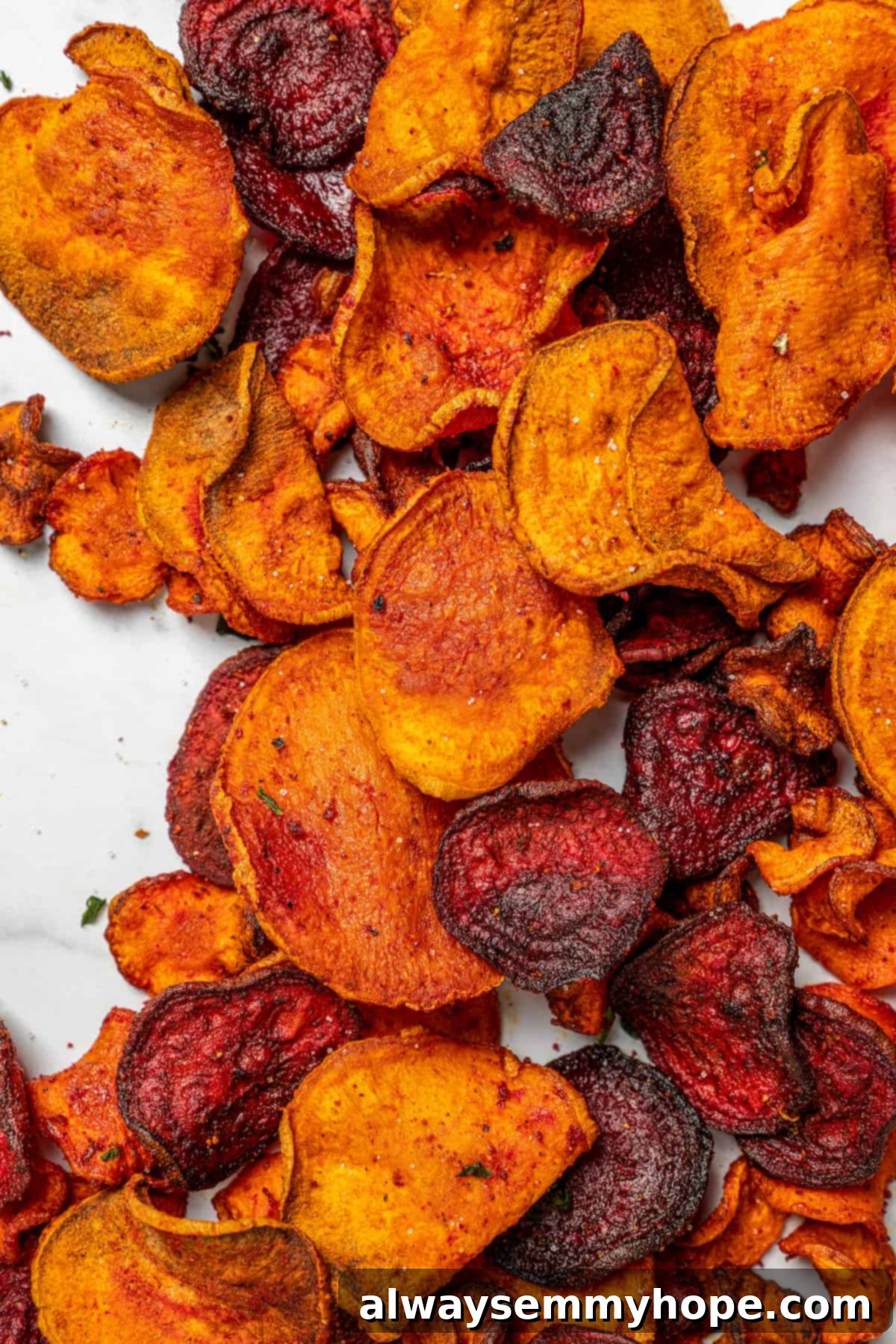 An inviting overhead view of a generous portion of crispy air fryer veggie chips spread across a clean marble countertop, highlighting their texture and vibrant colors.