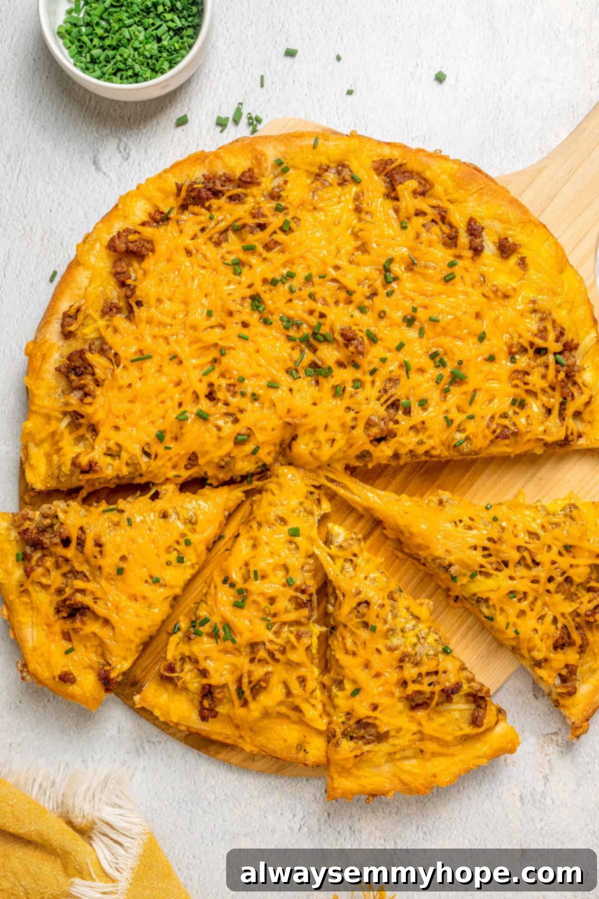 This vegan breakfast pizza features plant-based eggs, cheese, hash browns, and sausage, all baked on a crispy, chewy crust. So good! An overhead view of a freshly baked vegan breakfast pizza on a wooden board, with four slices already cut and ready to serve. The pizza is topped with plant-based eggs, cheese, hash browns, and sausage.