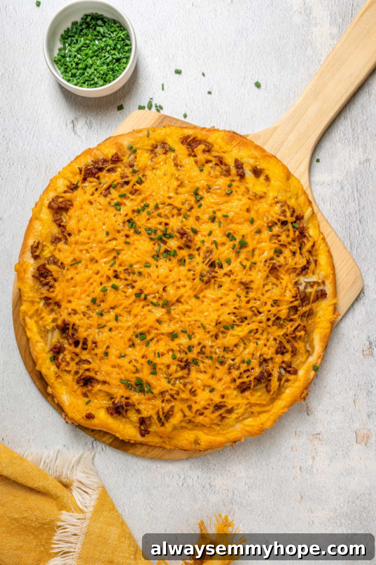 This vegan breakfast pizza features plant-based eggs, cheese, hash browns, and sausage, all baked on a crispy, chewy crust. So good! An overhead shot of a golden-brown vegan breakfast pizza on a rustic wooden pizza board, freshly baked and whole, waiting to be sliced.