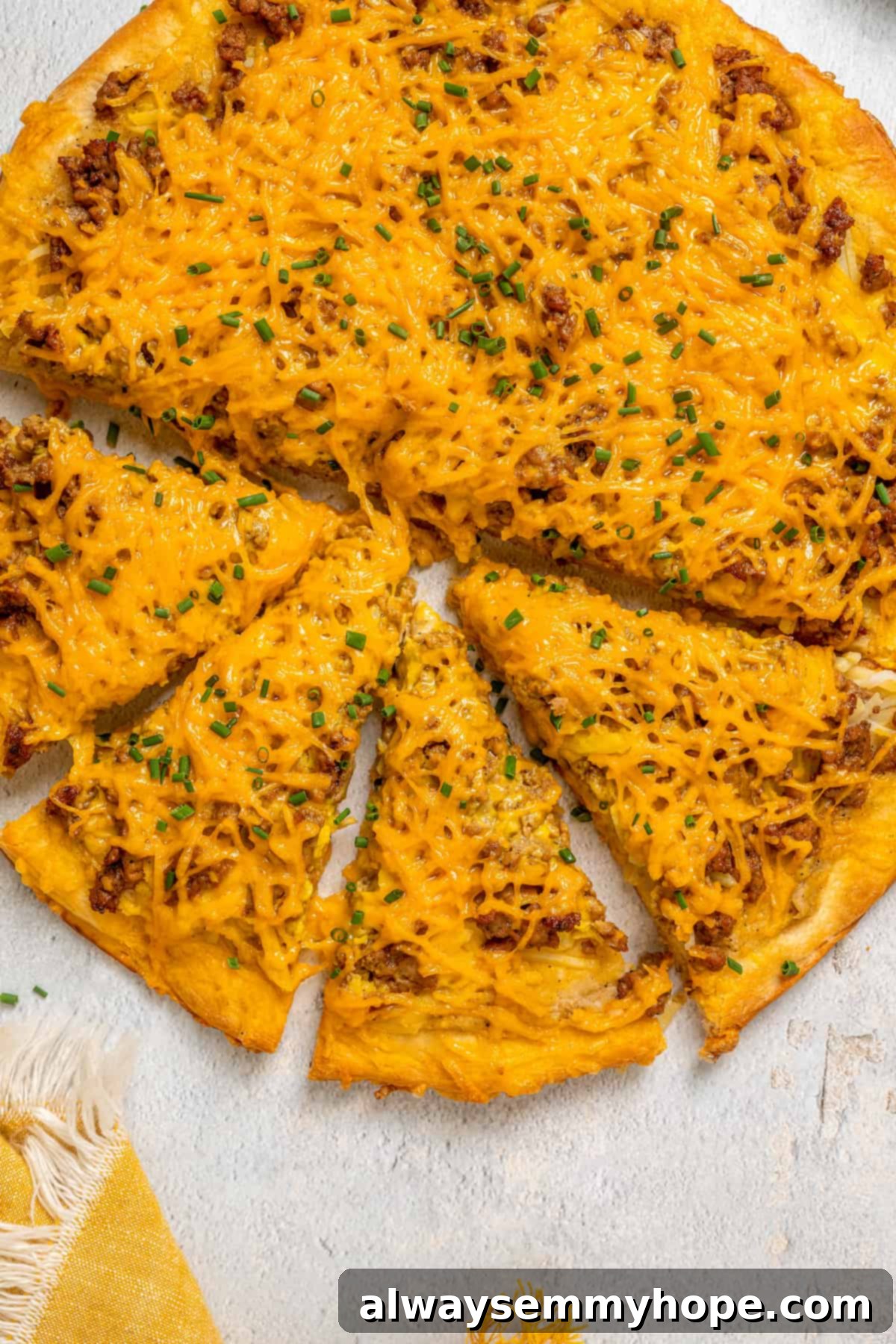 This vegan breakfast pizza features plant-based eggs, cheese, hash browns, and sausage, all baked on a crispy, chewy crust. So good! Overhead view of a vegan breakfast pizza on a wooden board, with four slices already cut, garnished with fresh chives, and ready to be served.