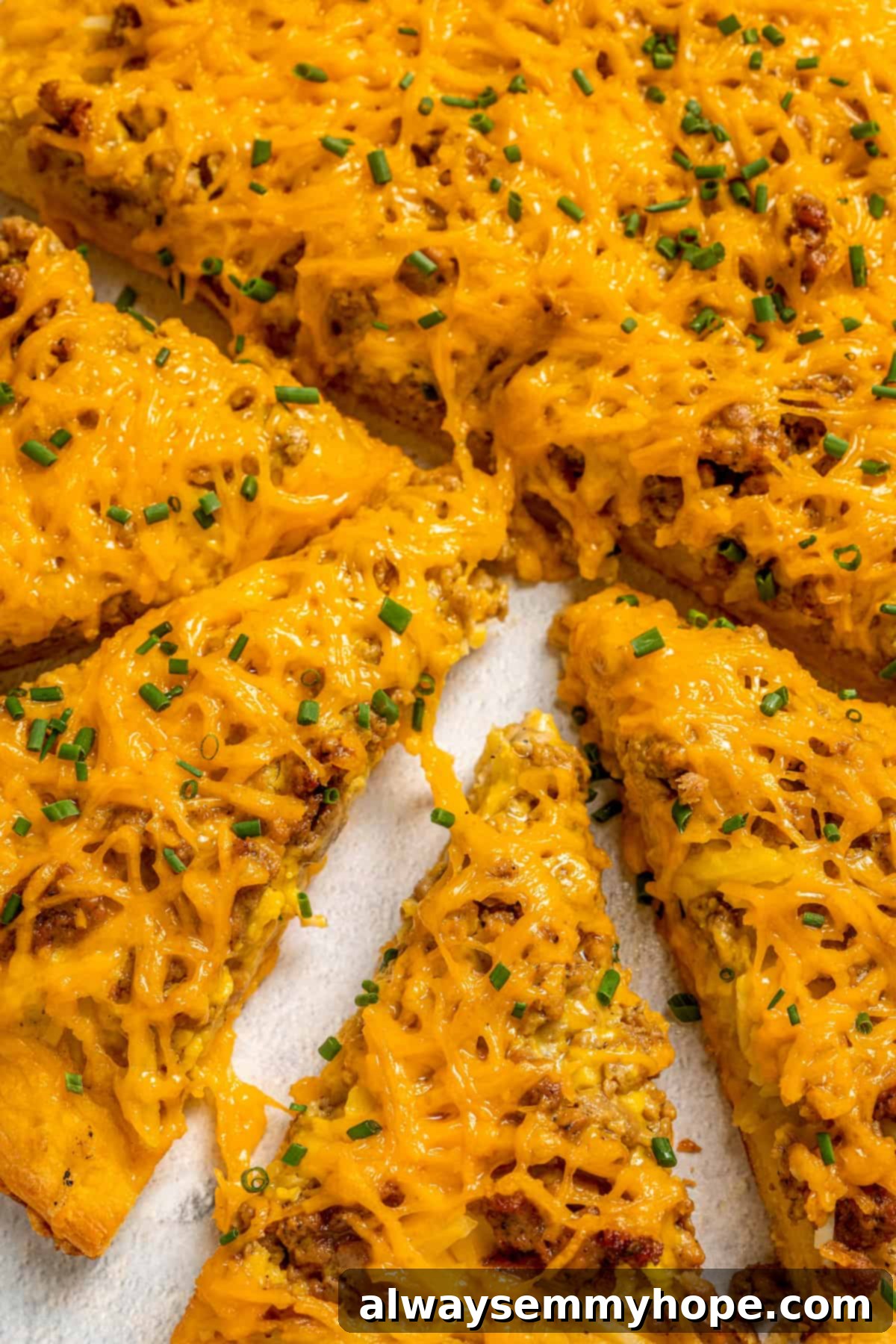 This vegan breakfast pizza features plant-based eggs, cheese, hash browns, and sausage, all baked on a crispy, chewy crust. So good! A close-up view of a cut vegan breakfast pizza on a wooden board, with one slice pulled away to reveal the layers of plant-based egg, cheese, hash browns, and sausage.