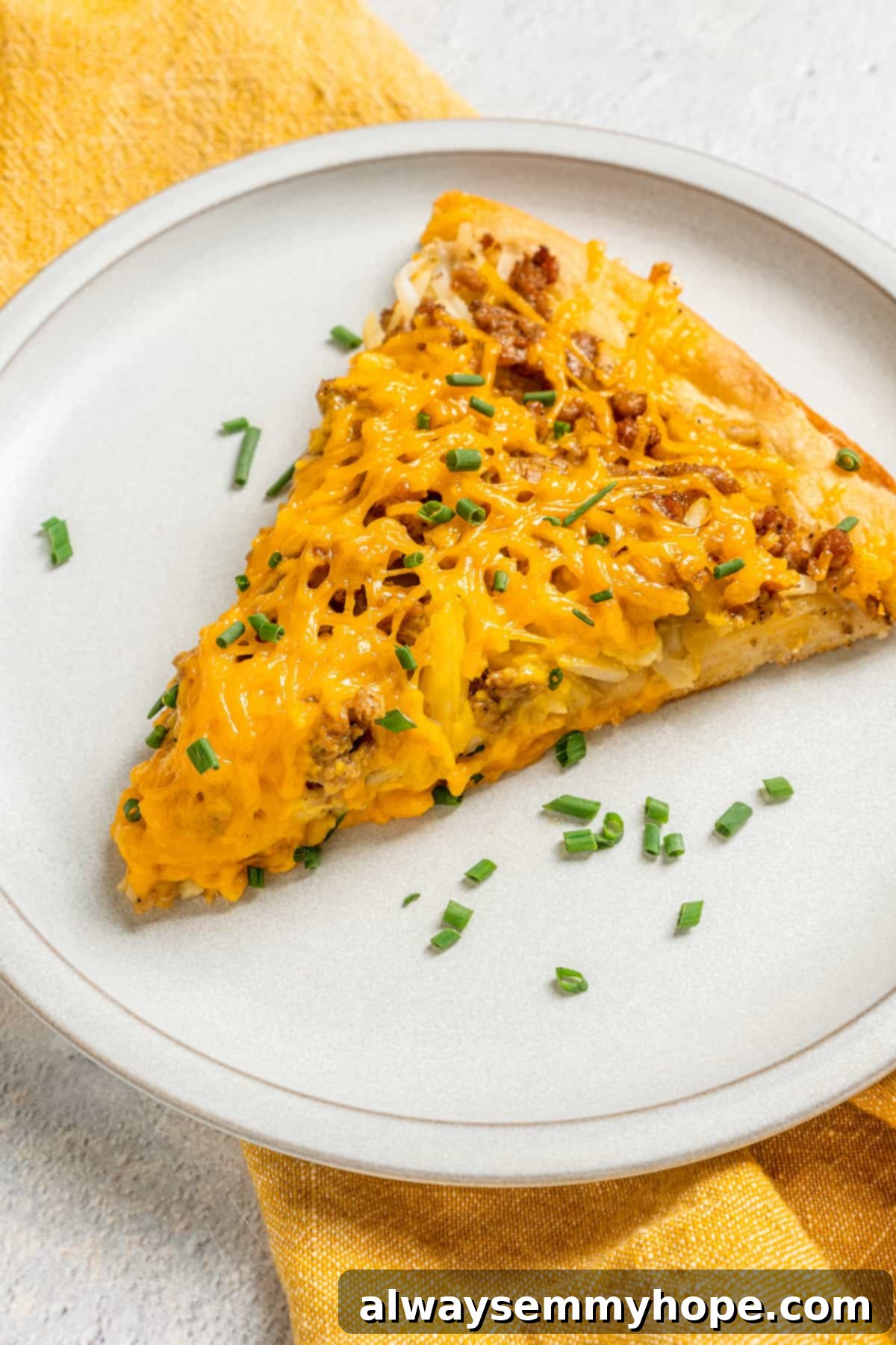 This vegan breakfast pizza features plant-based eggs, cheese, hash browns, and sausage, all baked on a crispy, chewy crust. So good! A single slice of vegan breakfast pizza on a white plate, topped with fresh green chives, ready to be eaten. It showcases the crispy crust and layered toppings.